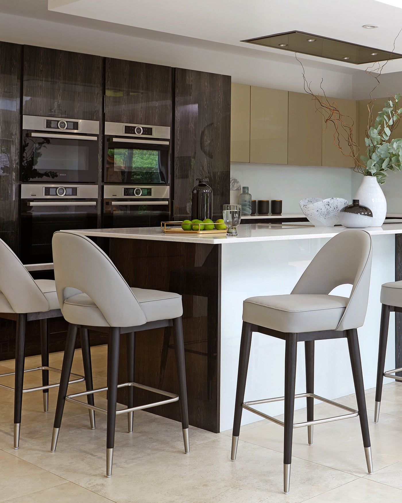 Elegant modern kitchen bar stools with dark wooden legs and sleek grey upholstery, enhanced by metallic footrests and positioned around a white kitchen island.