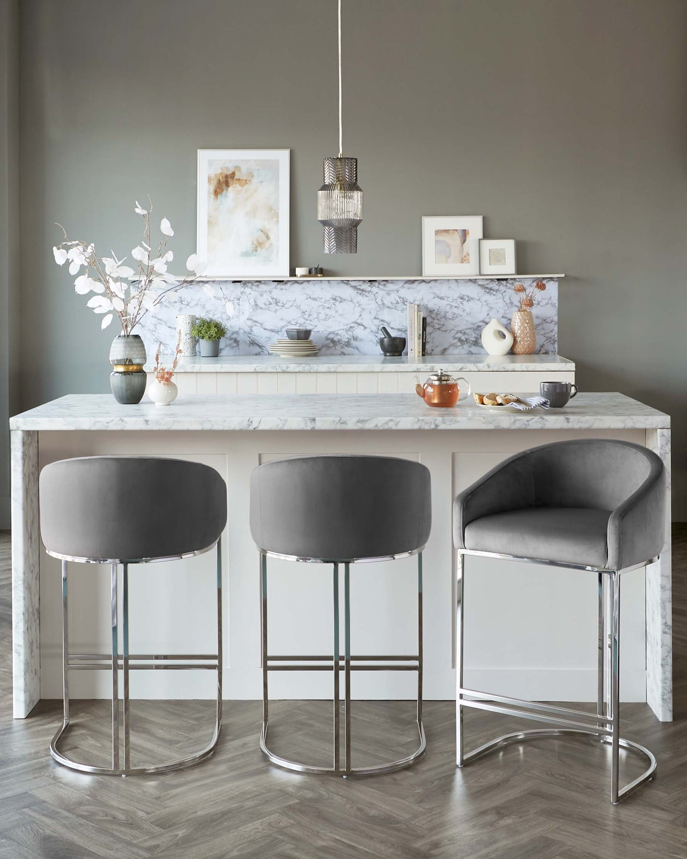 Two modern grey upholstered bar stools with sleek chrome bases in front of a marble kitchen counter.