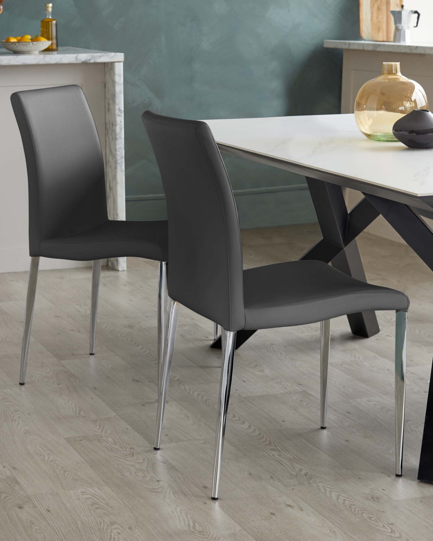 Modern dining furniture set featuring a white marble table with a distinctive black angular base, paired with sleek black upholstered chairs that have chrome-finished metal legs.