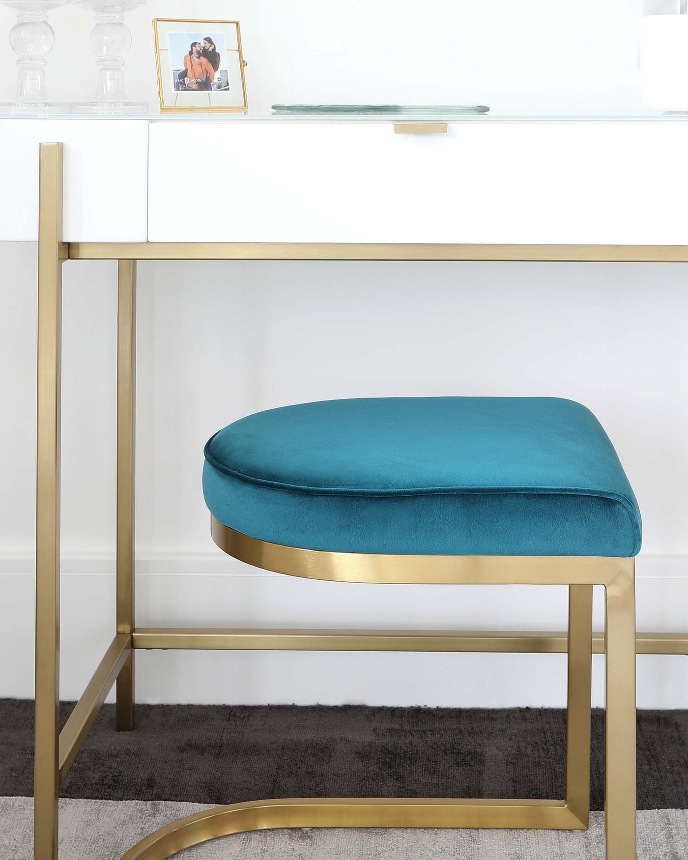 Elegant modern furniture featuring a white minimalist desk with a sleek golden frame and a plush teal velvet ottoman with a matching golden base.