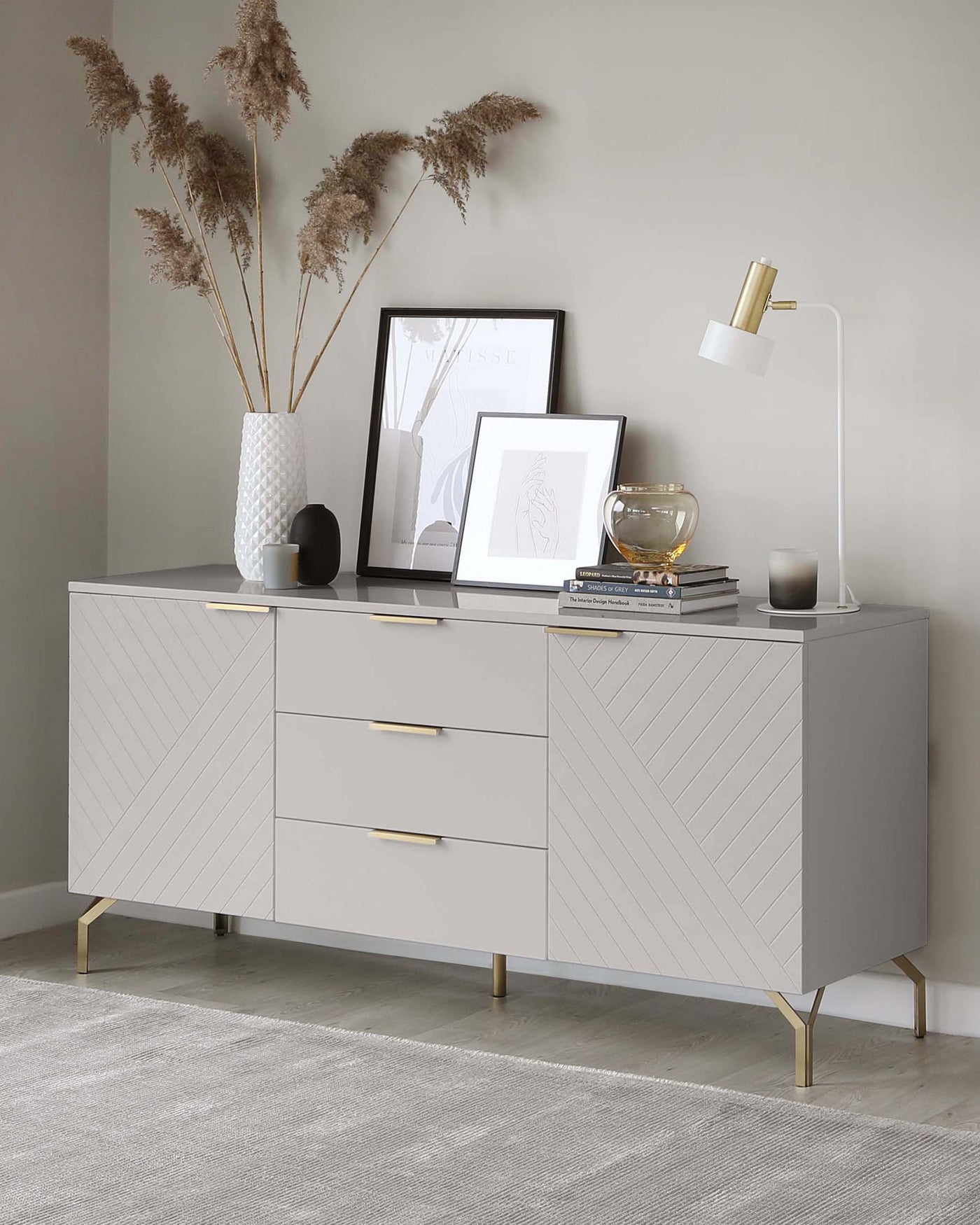 Modern light grey sideboard with geometric line detailing and brass handles and legs, styled with decorative objects and artwork on top.