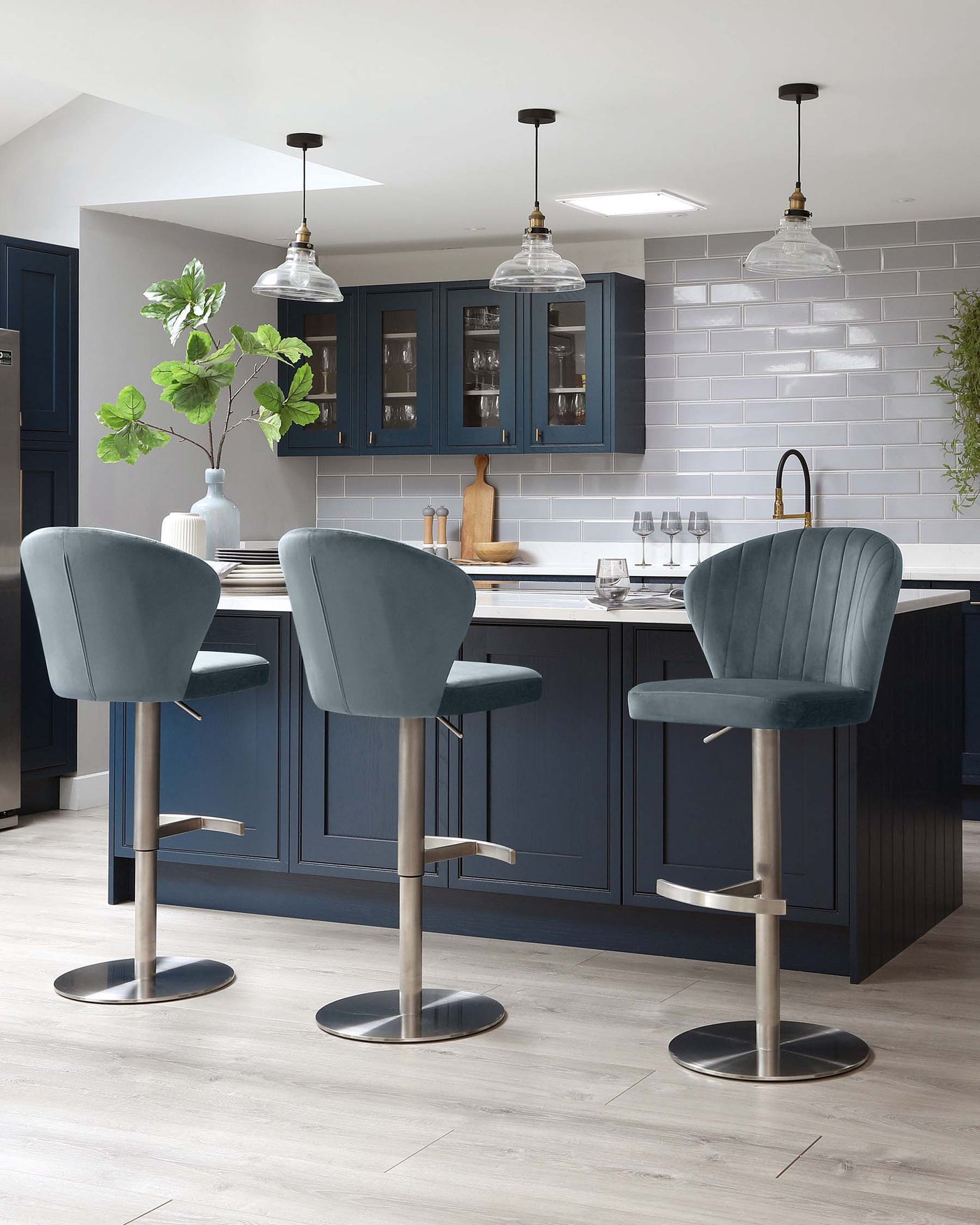 Modern kitchen with three elegant upholstered bar stools featuring curved backs and plush seating, supported by sleek metallic pedestals and circular bases.