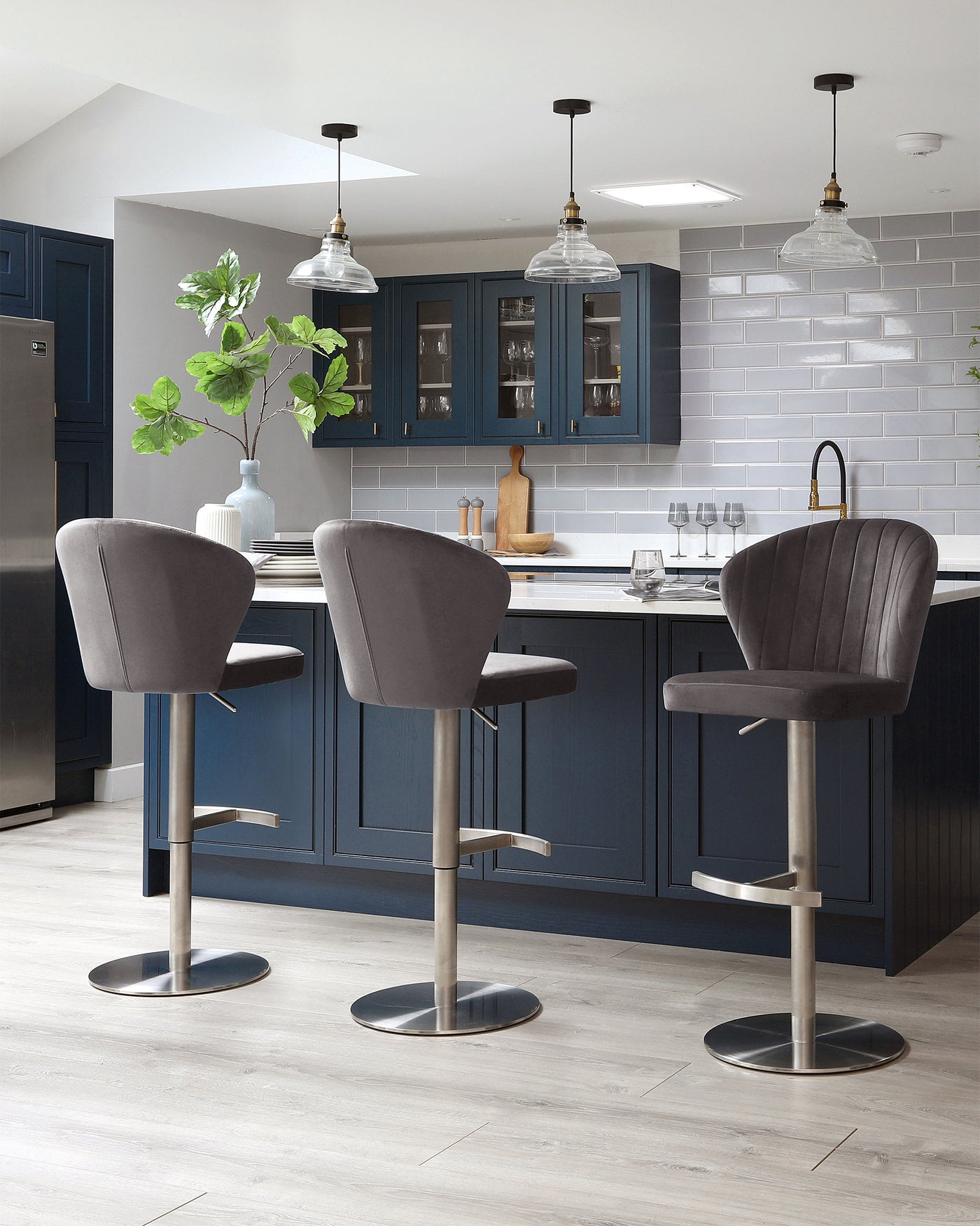 Three modern bar stools with grey upholstery and padded seats, featuring high-backs with channel tufting. These stools have sleek, adjustable metal bases with built-in footrests, giving off a contemporary aesthetic perfect for kitchen islands or home bars.
