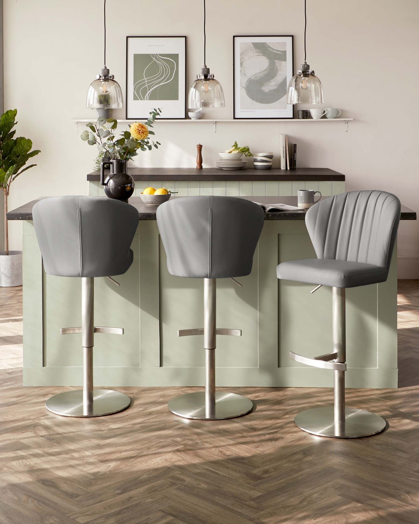 Three modern grey upholstered bar stools with tufted backrests and adjustable stainless steel bases, positioned around a light green kitchen island.