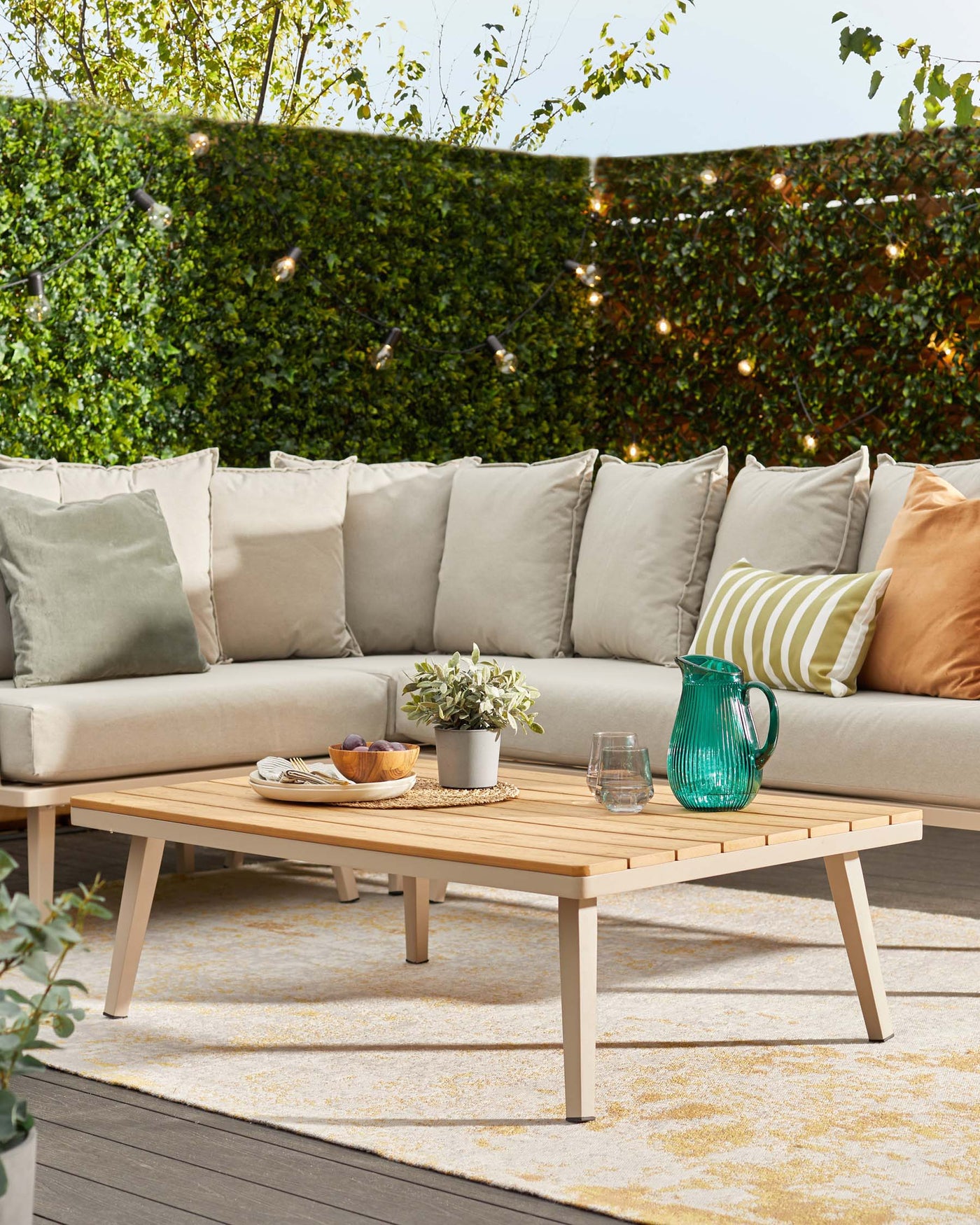Outdoor lounge setting featuring a large beige modular sofa with plush cushions and a rectangular wooden coffee table with a slatted surface design.