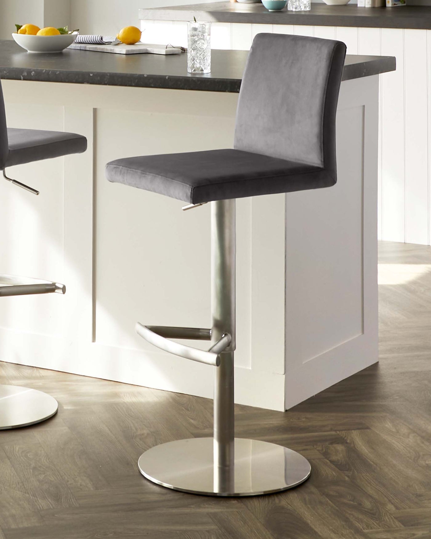 Modern adjustable bar stool with a sleek chrome pedestal base, featuring an integrated footrest. The seat and backrest are upholstered in a grey faux leather with a subtle horizontal stitching, providing a contemporary look suitable for a variety of kitchen interiors.