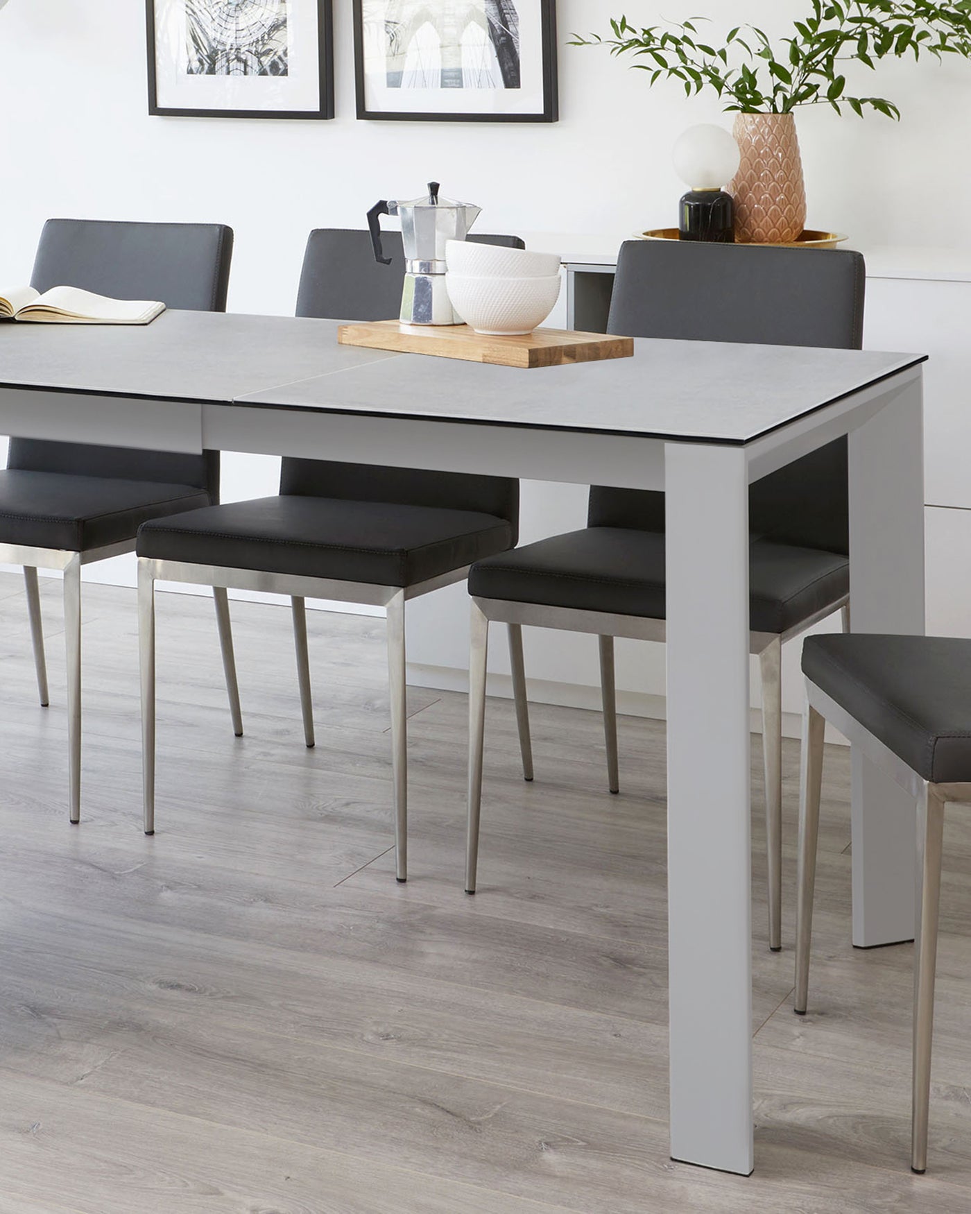 Modern minimalist dining set comprising a rectangular table with a light grey surface and white legs, surrounded by six matching dark upholstered chairs with slim metal legs.