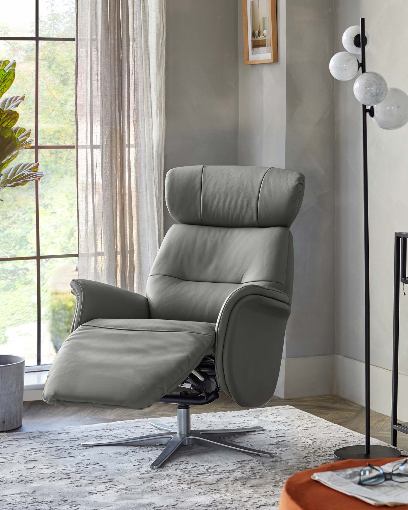Modern grey leather recliner chair with padded headrest and armrests, featuring a swivel base and an adjustable head tilt, showcased in a bright room with natural light.