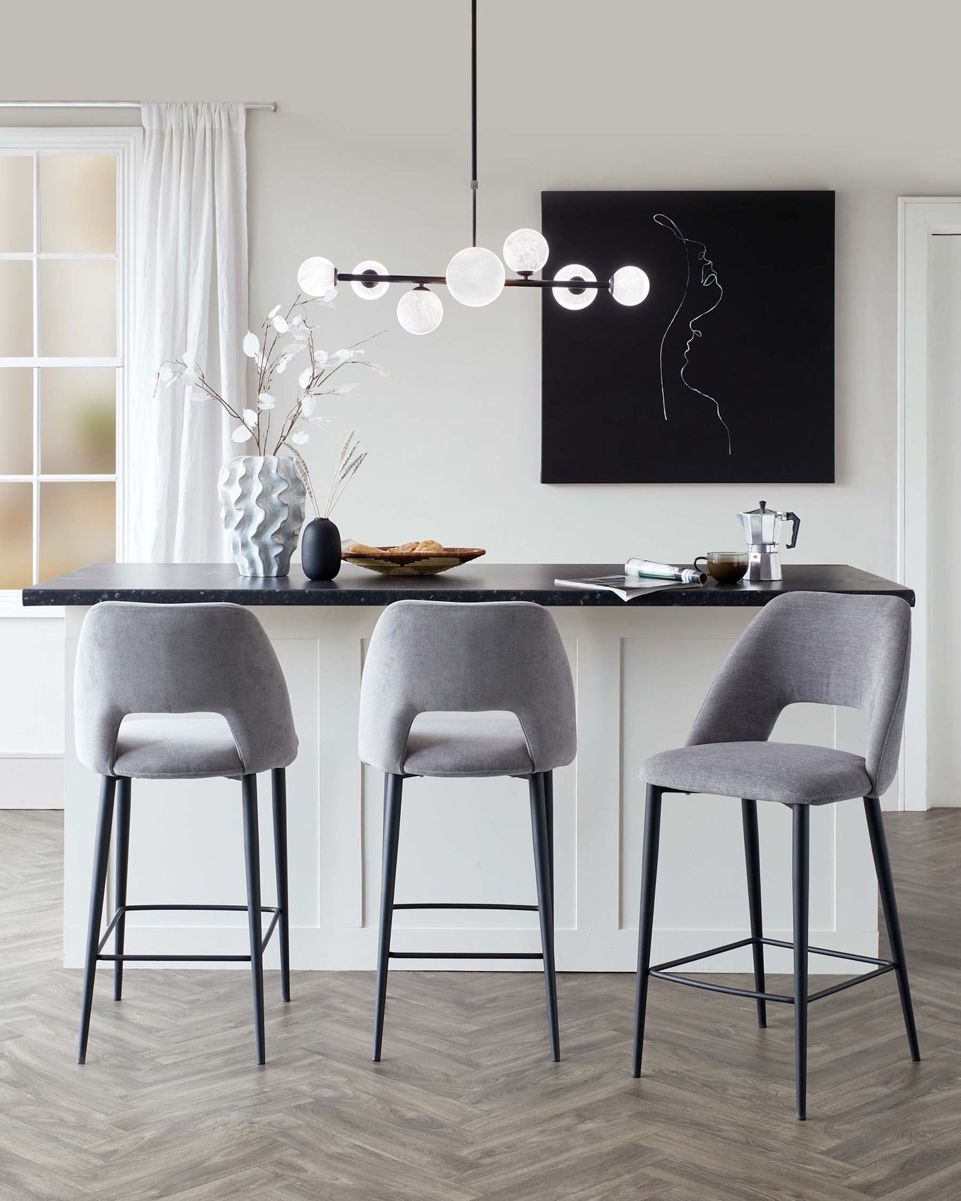 Modern minimalist kitchen with three contemporary bar stools featuring grey upholstery and slender black metal legs, paired with a sleek black countertop.