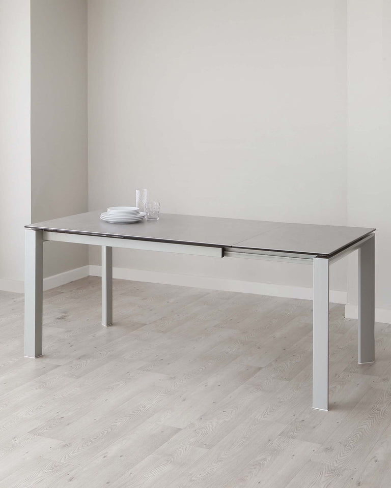 Modern minimalist extendable dining table with a light grey tabletop and sleek silver metal legs, set against a neutral background with a simple place setting.