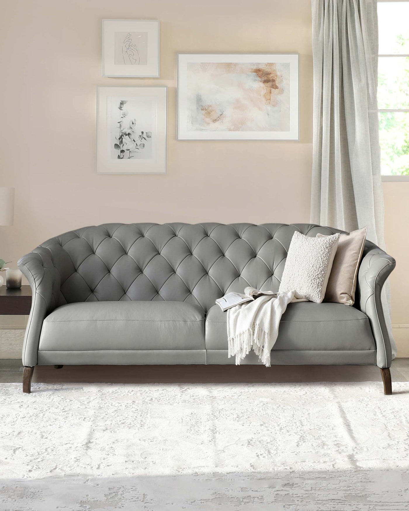 Elegant classic-style tufted sofa in light grey upholstery, featuring a curvaceous backrest and arms, with dark wooden legs. The sofa is accessorized with a textured throw blanket and a decorative cushion.