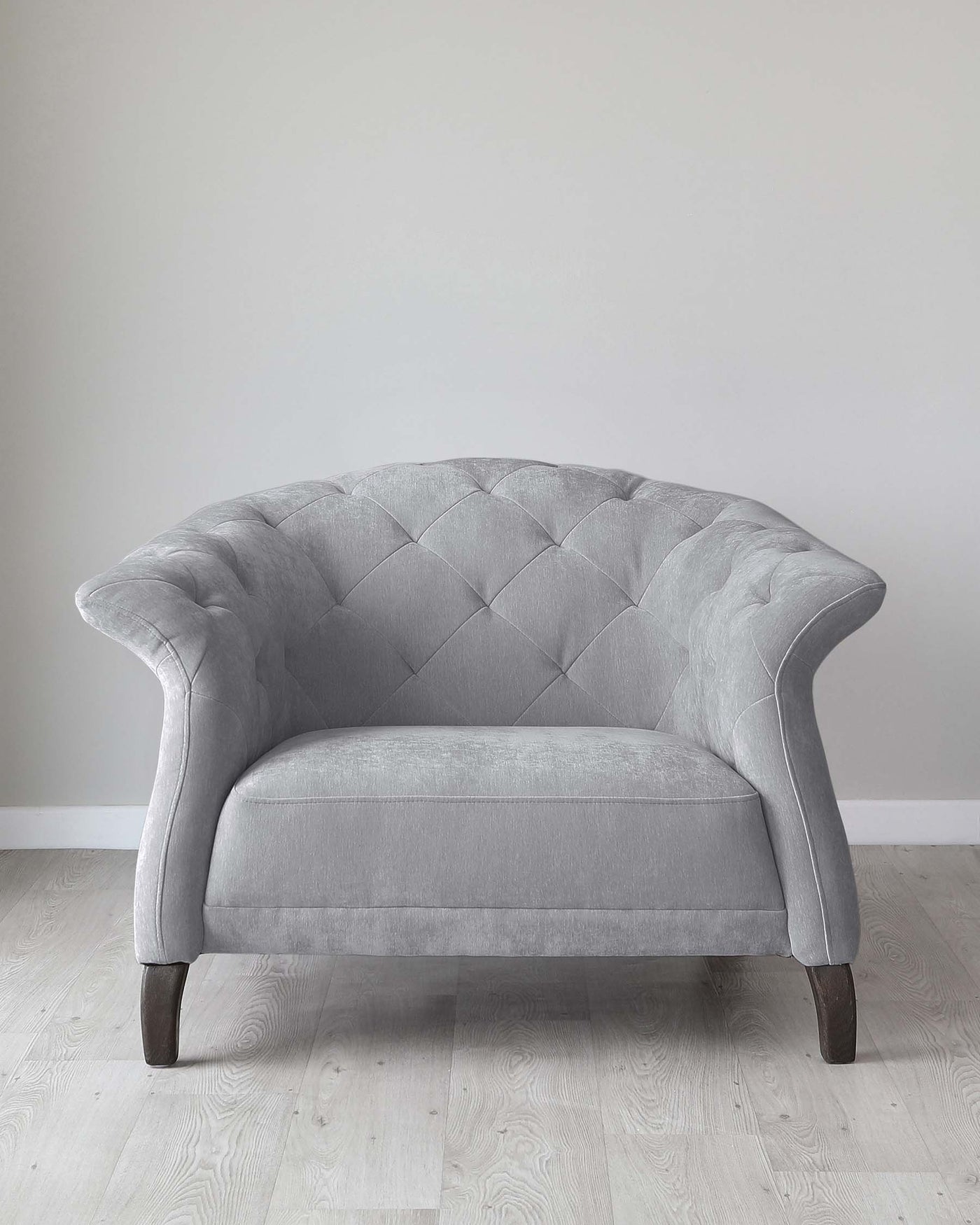 Elegant grey fabric loveseat with button-tufted backrest, curved armrests, and dark stained wooden legs standing on a light hardwood floor against a neutral wall.