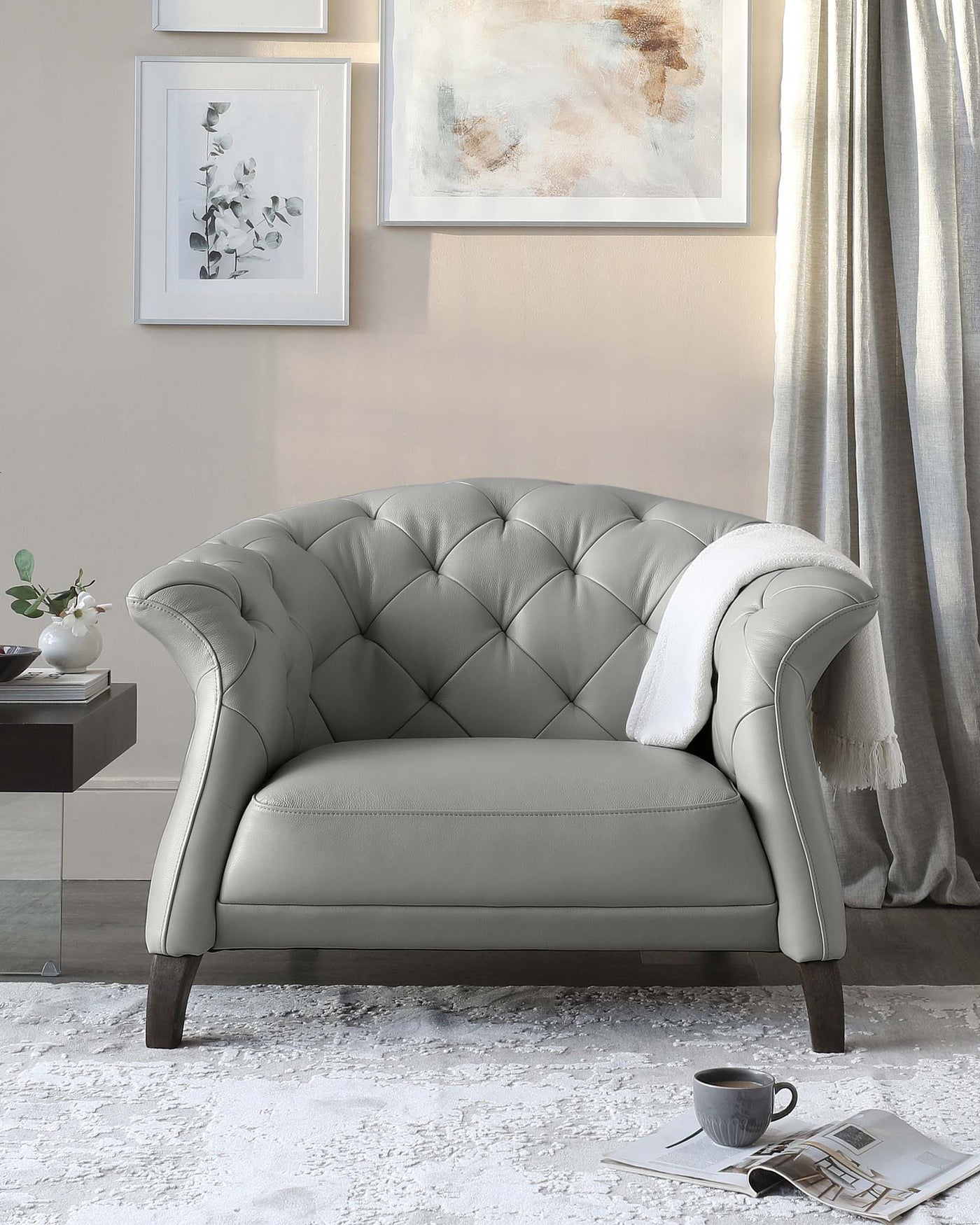 Elegant grey tufted loveseat with a plush, curved back, dark wooden legs, and a soft white throw blanket on one armrest, set in a stylishly decorated room.