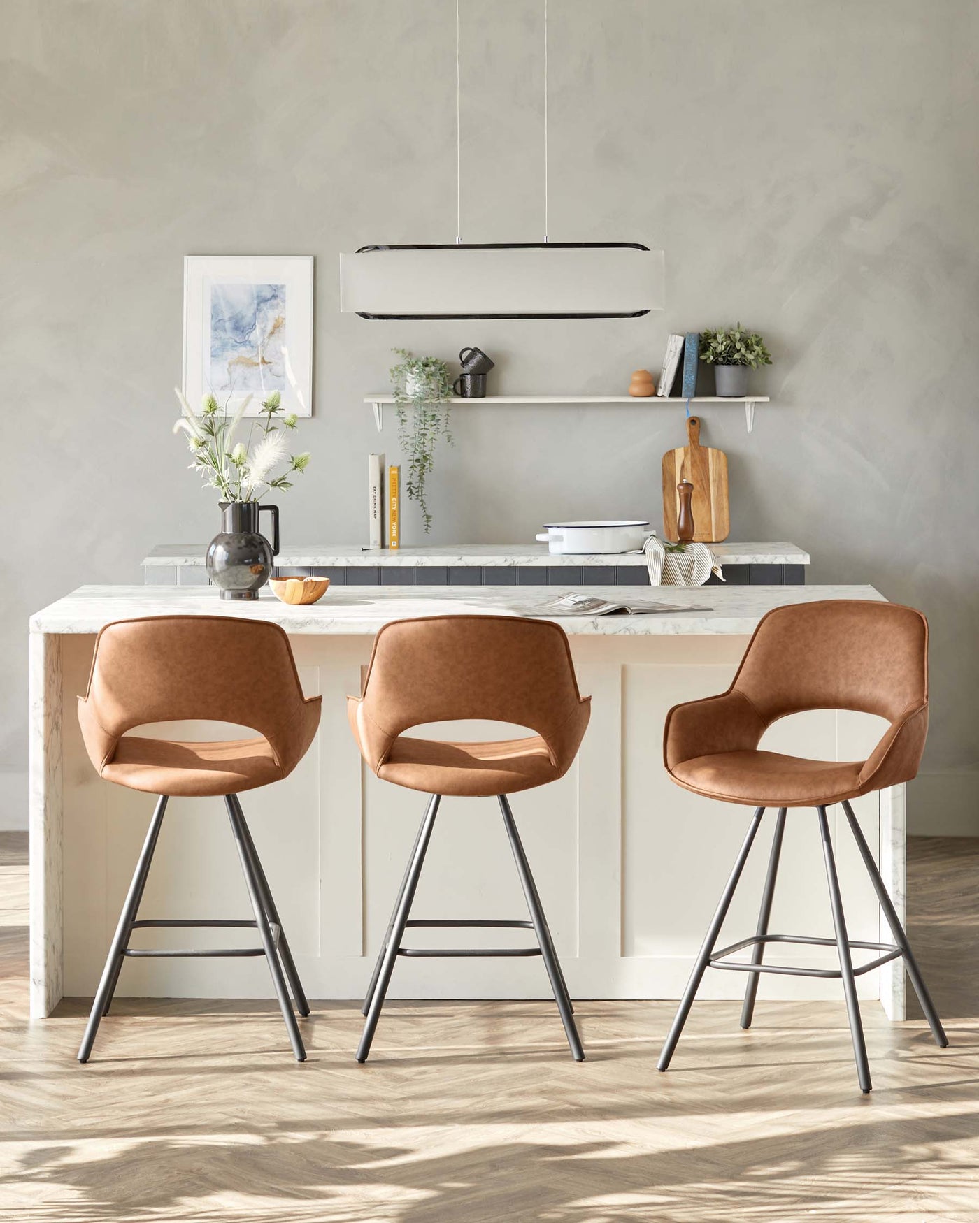 Modern kitchen interior featuring two elegant caramel-brown upholstered bar chairs with curved backrests and slender metallic legs, complementing a white marble-topped kitchen island.
