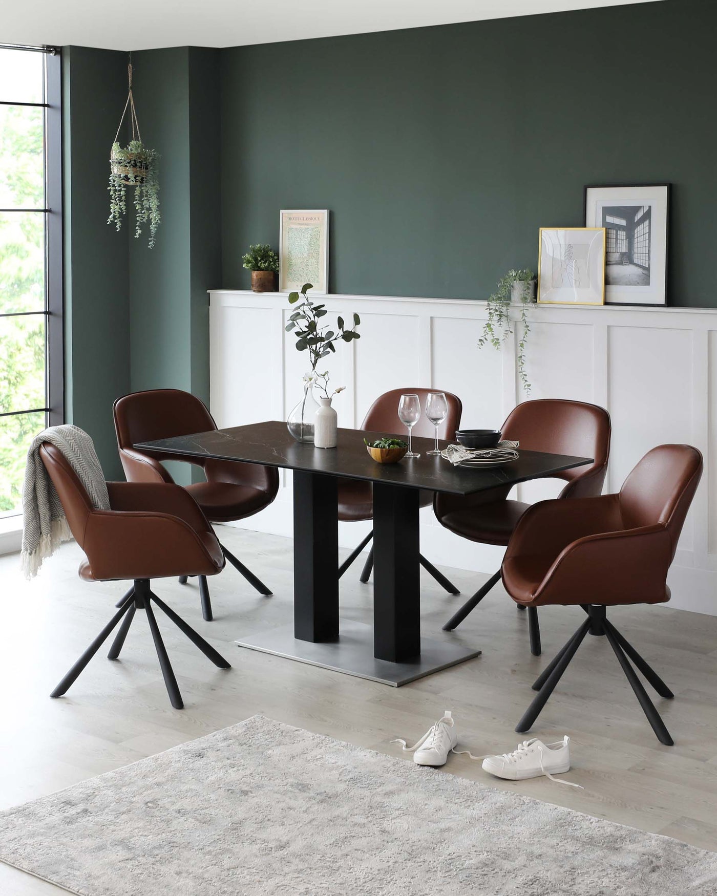 Modern dining room featuring a sleek rectangular table with a dark wood finish and bold black legs, surrounded by four elegant leather-upholstered chairs with black metal legs. A cosy beige rug underlays the set-up.