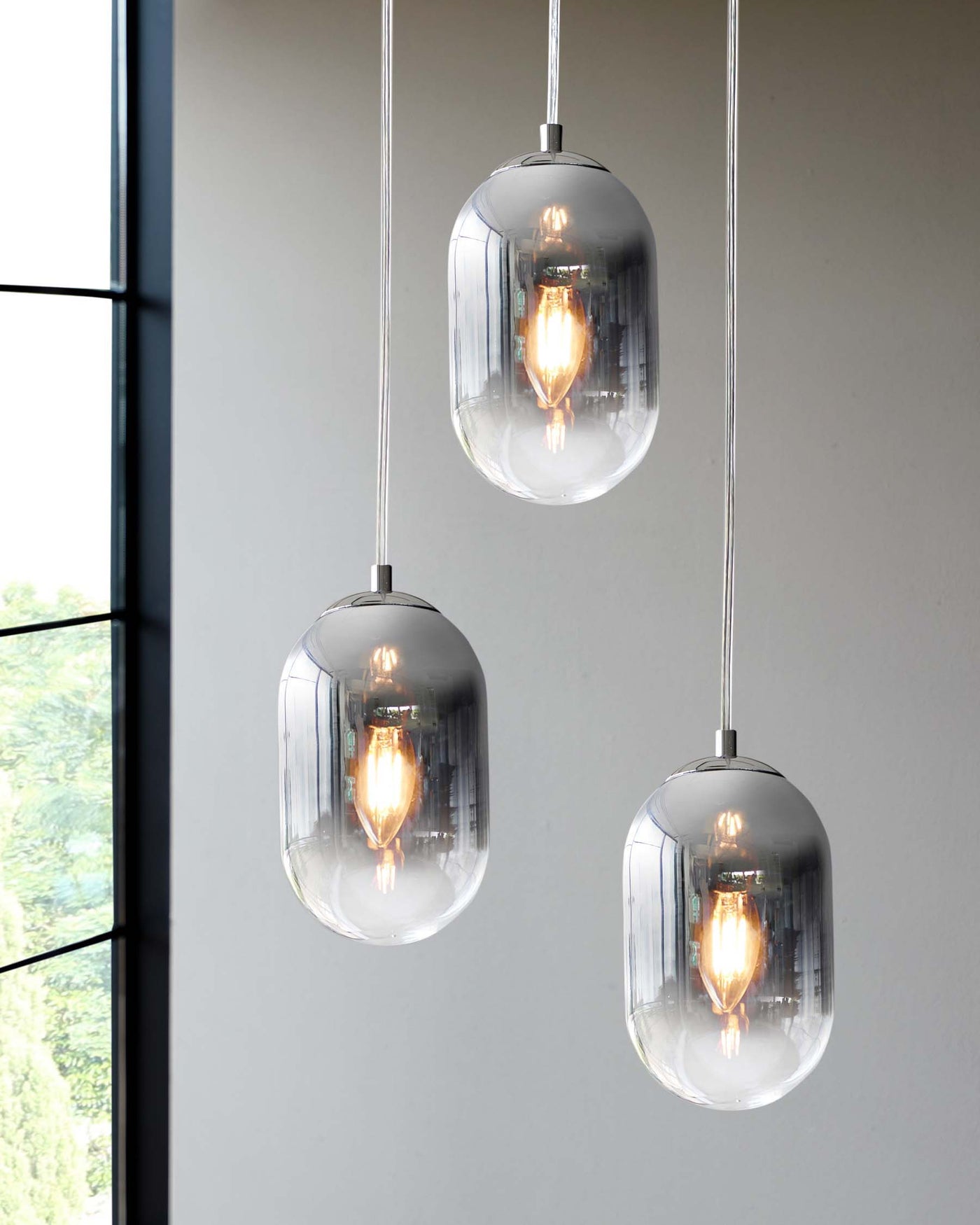 Three modern pendant lights with sleek oval-shaped, clear glass shades suspended by cords from a ceiling, each housing a luminous filament bulb.