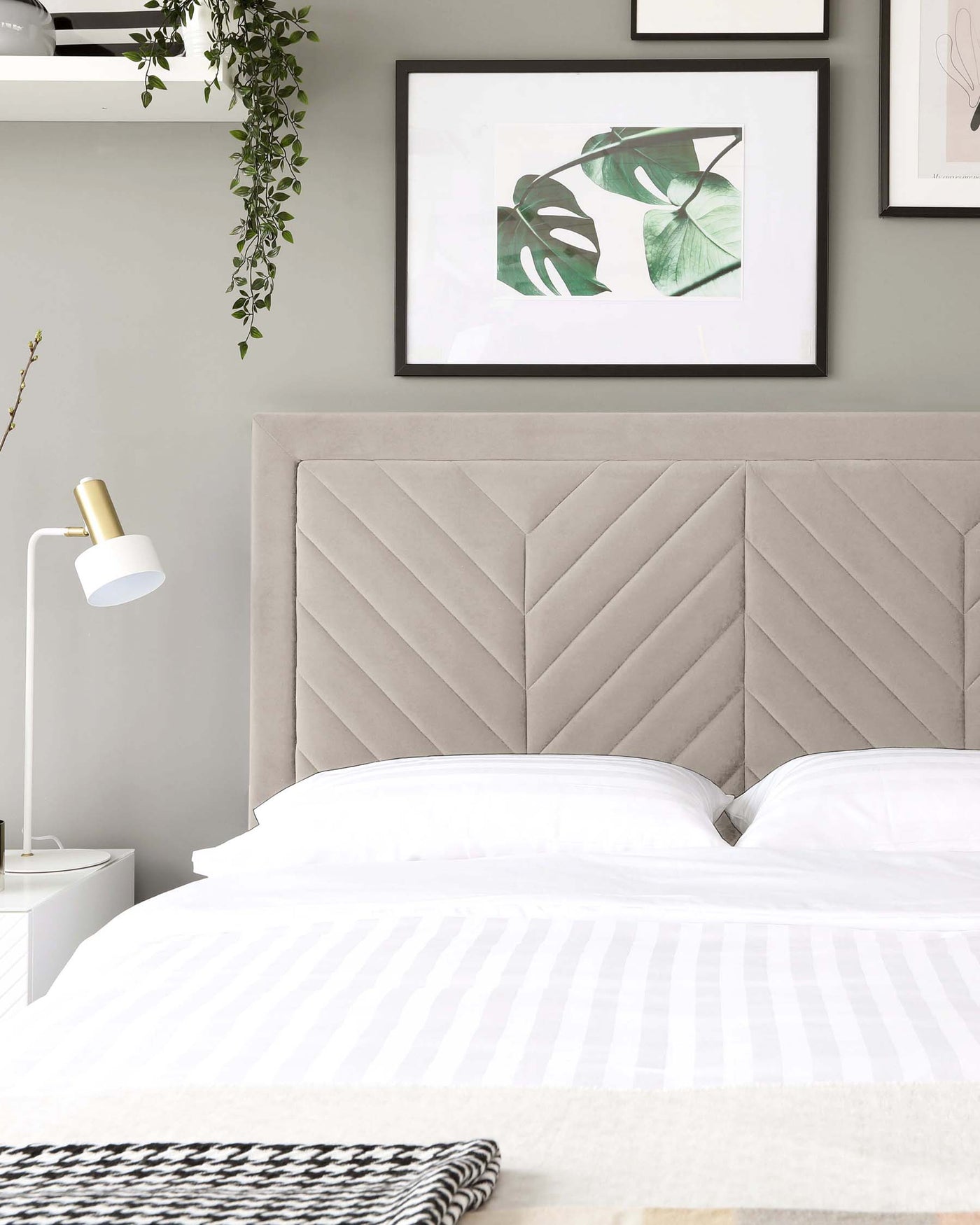 Elegant taupe upholstered bed with a herringbone-patterned headboard, white bedding, and a minimalist white bedside table with a modern white and gold lamp.