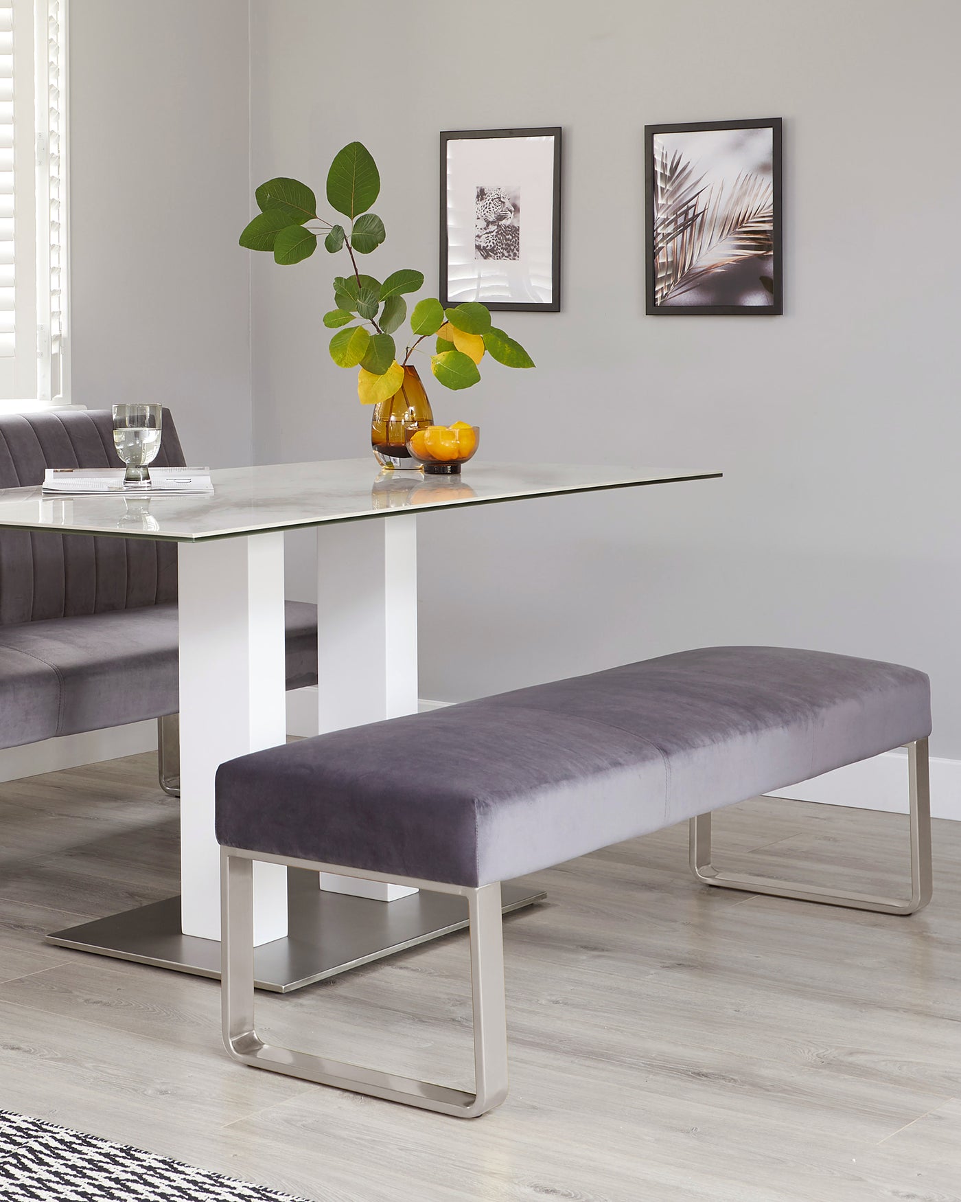 Modern dining furniture set featuring a sleek rectangular glass tabletop with white high-gloss legs, paired with a matching grey tufted upholstered bench with a unique U-shaped metallic base.