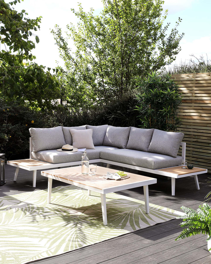 Outdoor furniture set featuring a modern corner sectional sofa with light grey cushions and a trio of white accent pillows, accompanied by two white-framed, wooden-topped coffee tables, set against a backdrop of lush greenery on a patio with a patterned area rug.