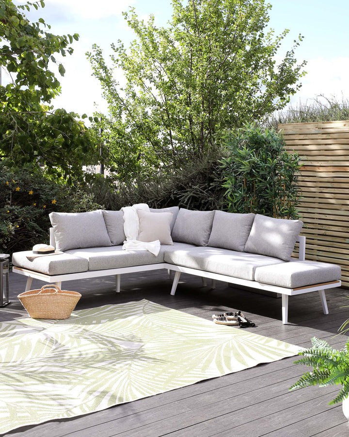Modern outdoor L-shaped sectional sofa with white aluminium frame and light grey cushions, accompanied by matching white throw pillows, set on a wooden deck with a patterned outdoor rug.