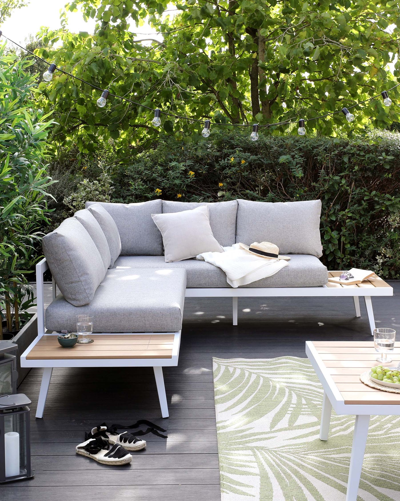 Outdoor contemporary furniture set consisting of a sleek white and grey sofa with comfortable grey cushions, accompanied by a white coffee table with a wooden tabletop. The set is arranged on a wooden deck with an accent of a patterned green outdoor rug, creating a cosy and inviting outdoor living space.