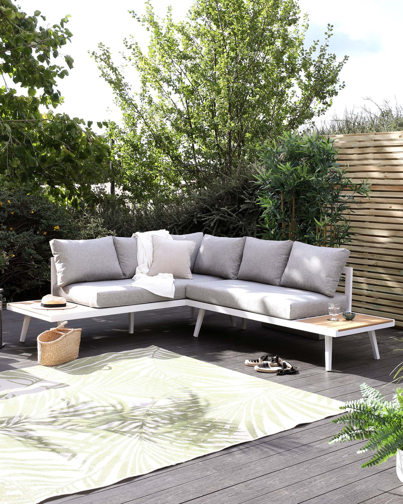 Outdoor sectional sofa with light grey cushions and a white frame, paired with a rectangular wooden coffee table on a patterned outdoor rug.