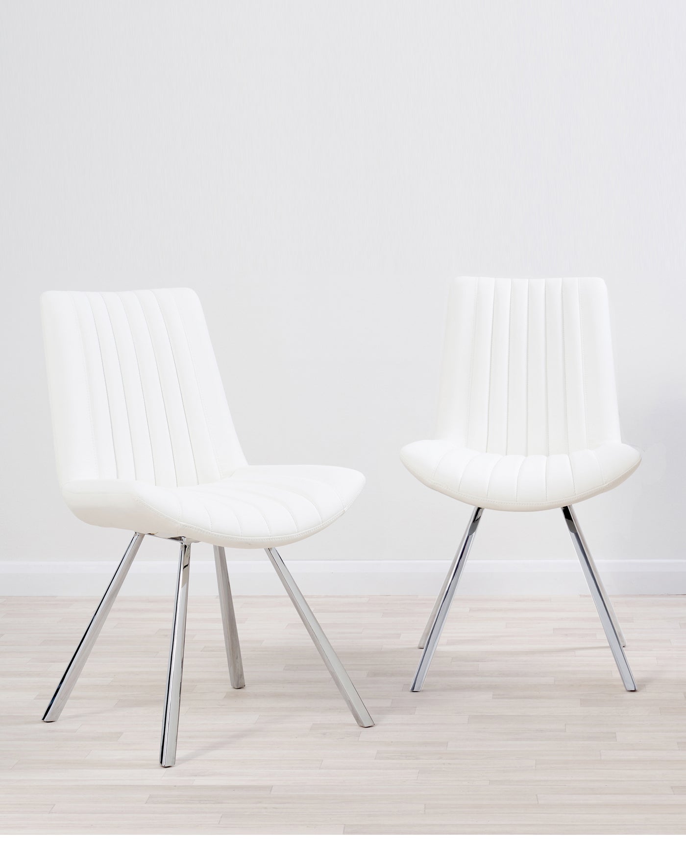 Two contemporary white upholstered dining chairs with vertical stitching detail on the backrest and seat cushion, set on sleek, angled chrome legs.