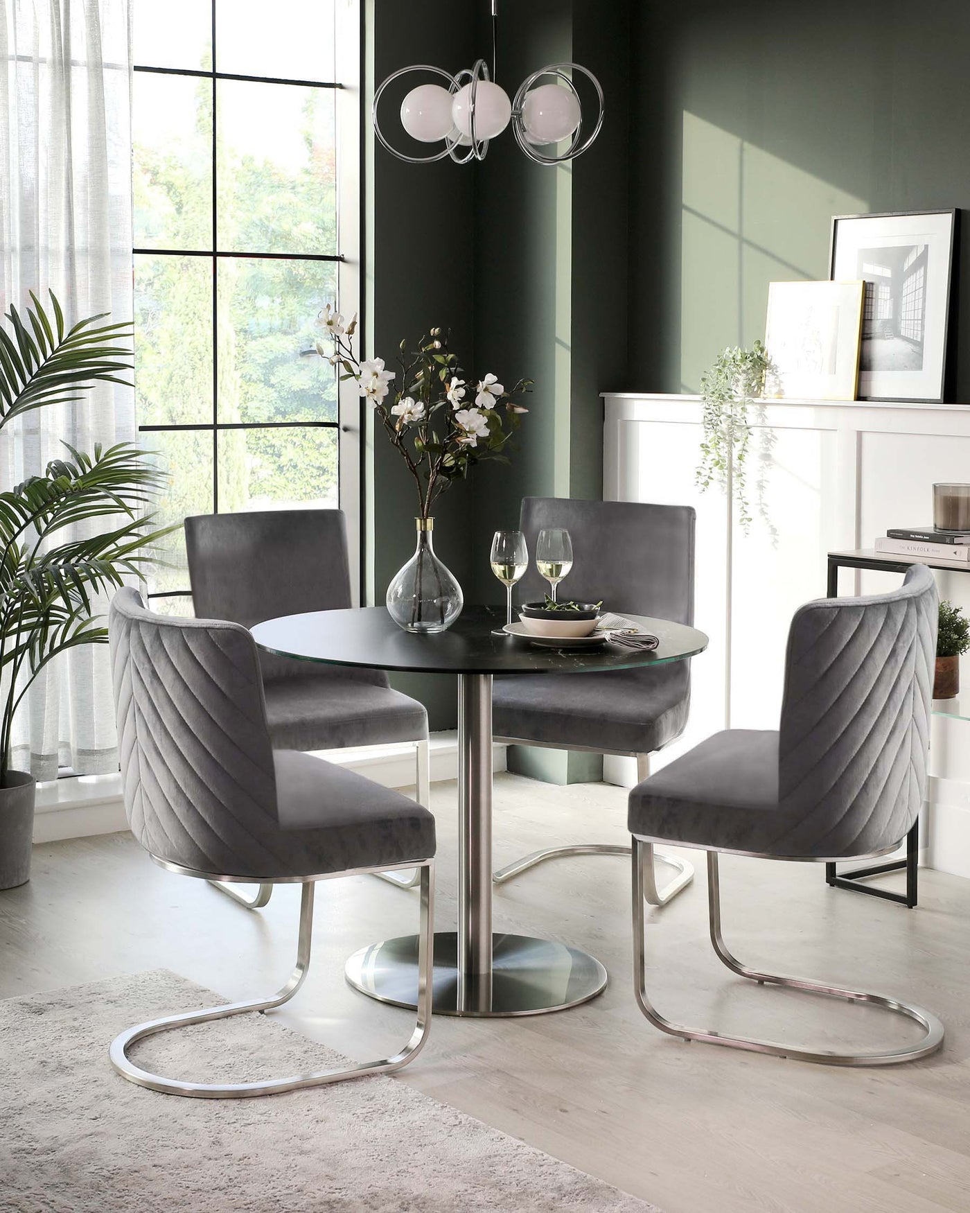 Elegant modern dining set featuring a round black table with a reflective cylindrical base and three grey velvet upholstered chairs with unique curved chrome legs. The set radiates sophistication and contemporary style, perfect for a chic dining room.