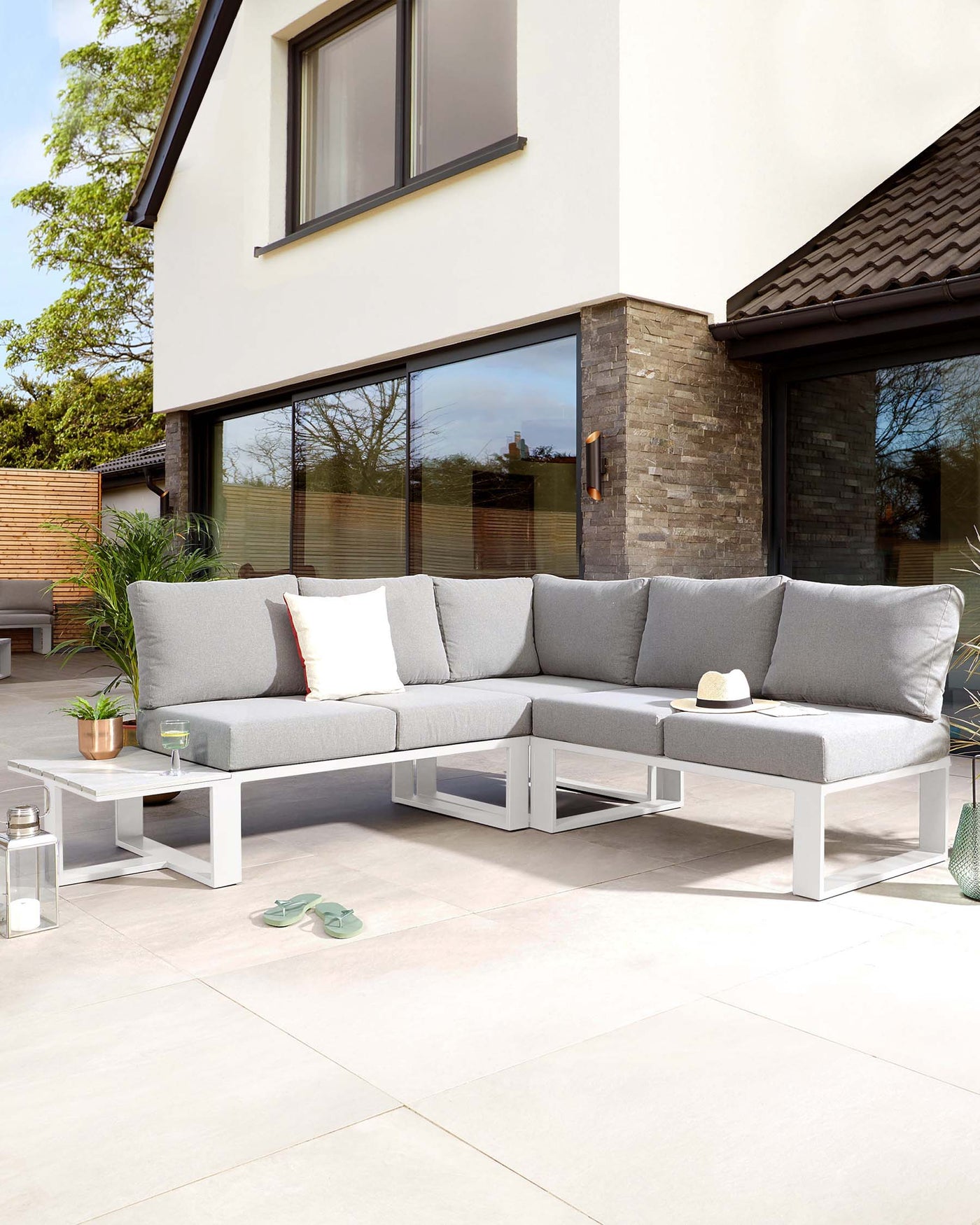Modern outdoor L-shaped sectional sofa with light grey cushions on a white minimalist frame, paired with a white square coffee table featuring a lower shelf.