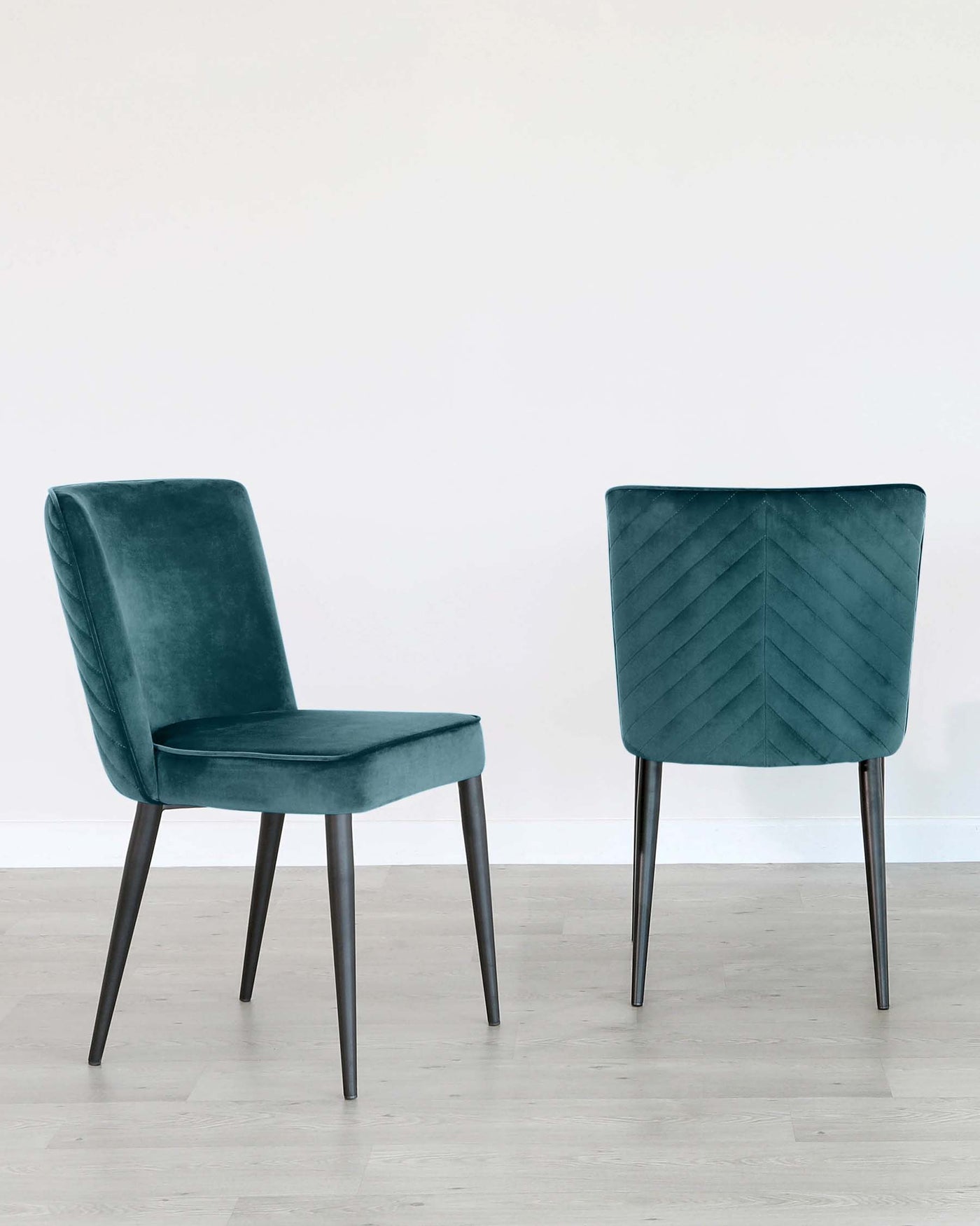 Two modern dining chairs with dark teal velvet upholstery and black metal legs, one featuring a smooth back and the other with a diagonally quilted back design.