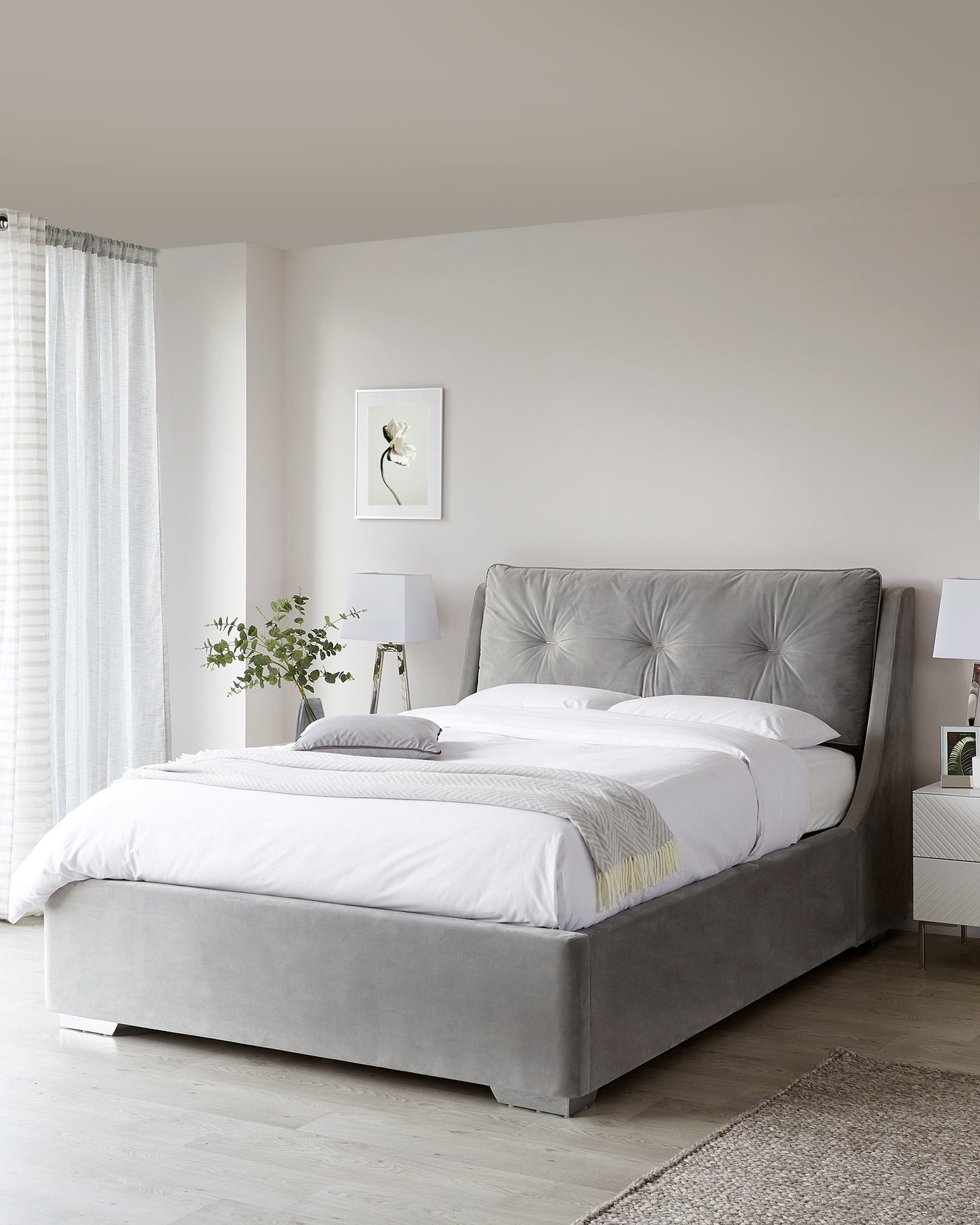 Elegant grey upholstered bed with tufted headboard and matching bed frame, complemented by white bedding and a light grey throw at the foot of the bed.