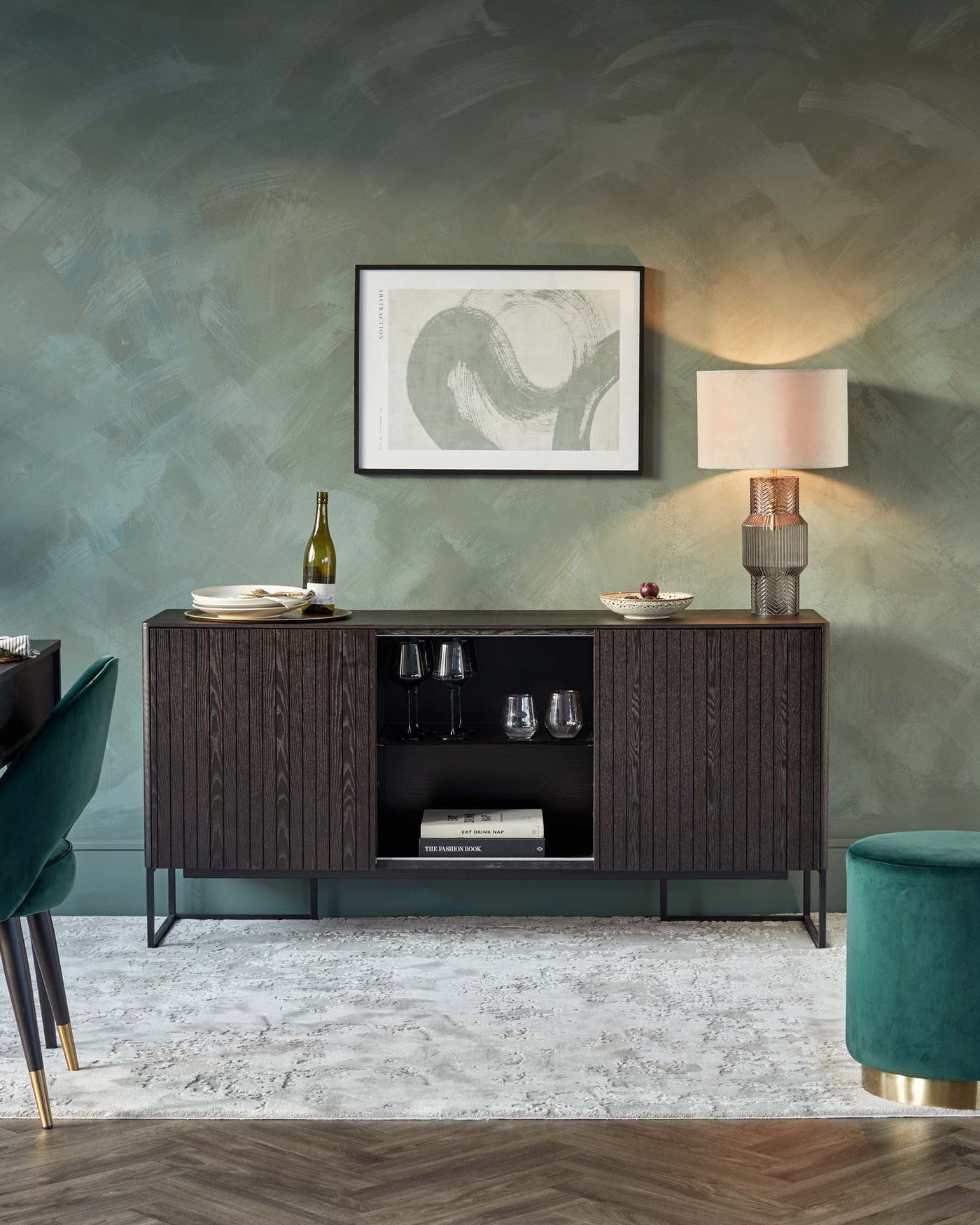 Elegant dark wood sideboard with patterned cabinet doors, central shelves, and metal legs, accompanied by a deep green, velvet-upholstered ottoman with a gold base.