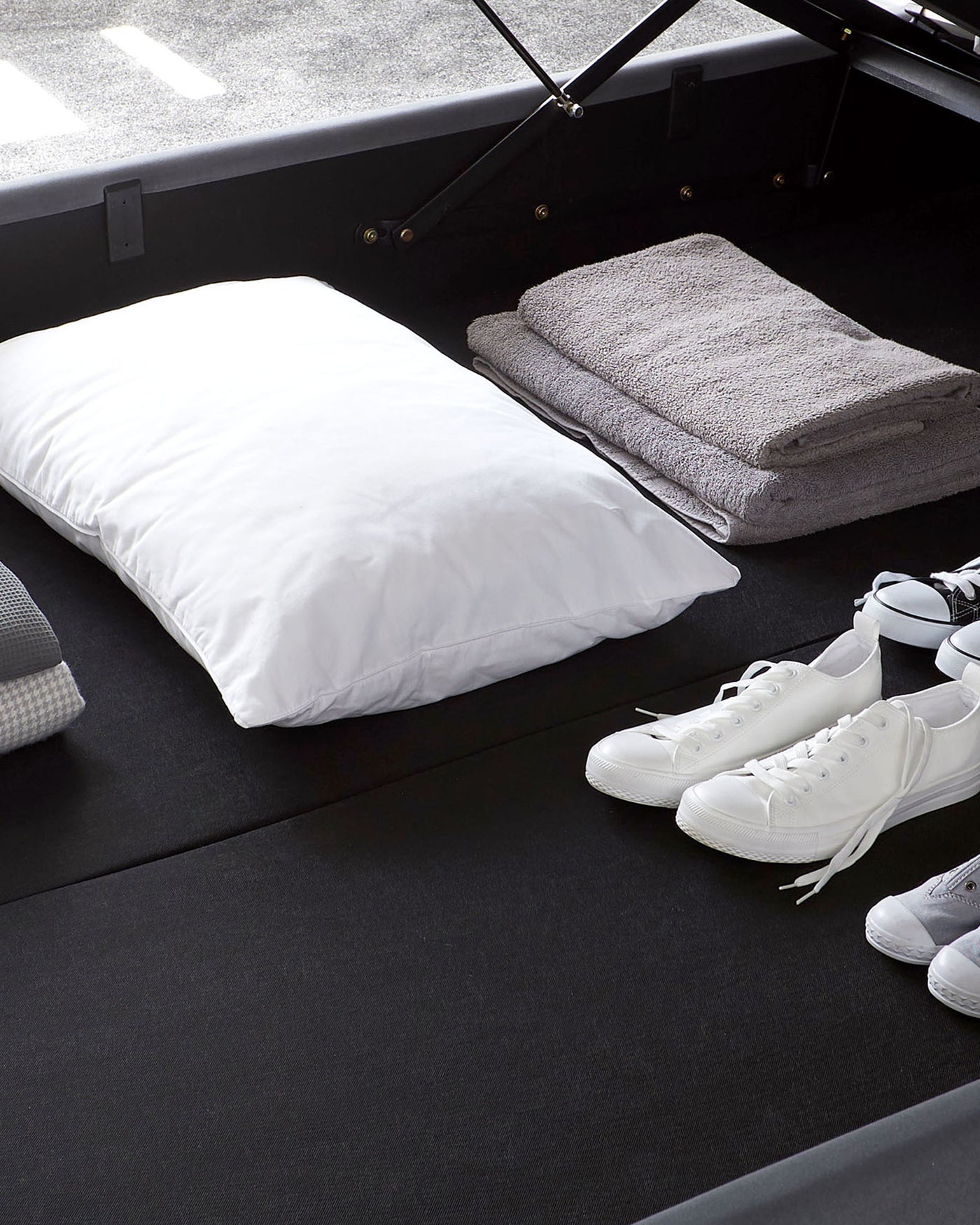 Black upholstered storage bed with gas-lift mechanism, displaying white linens and grey folded towels on one side.