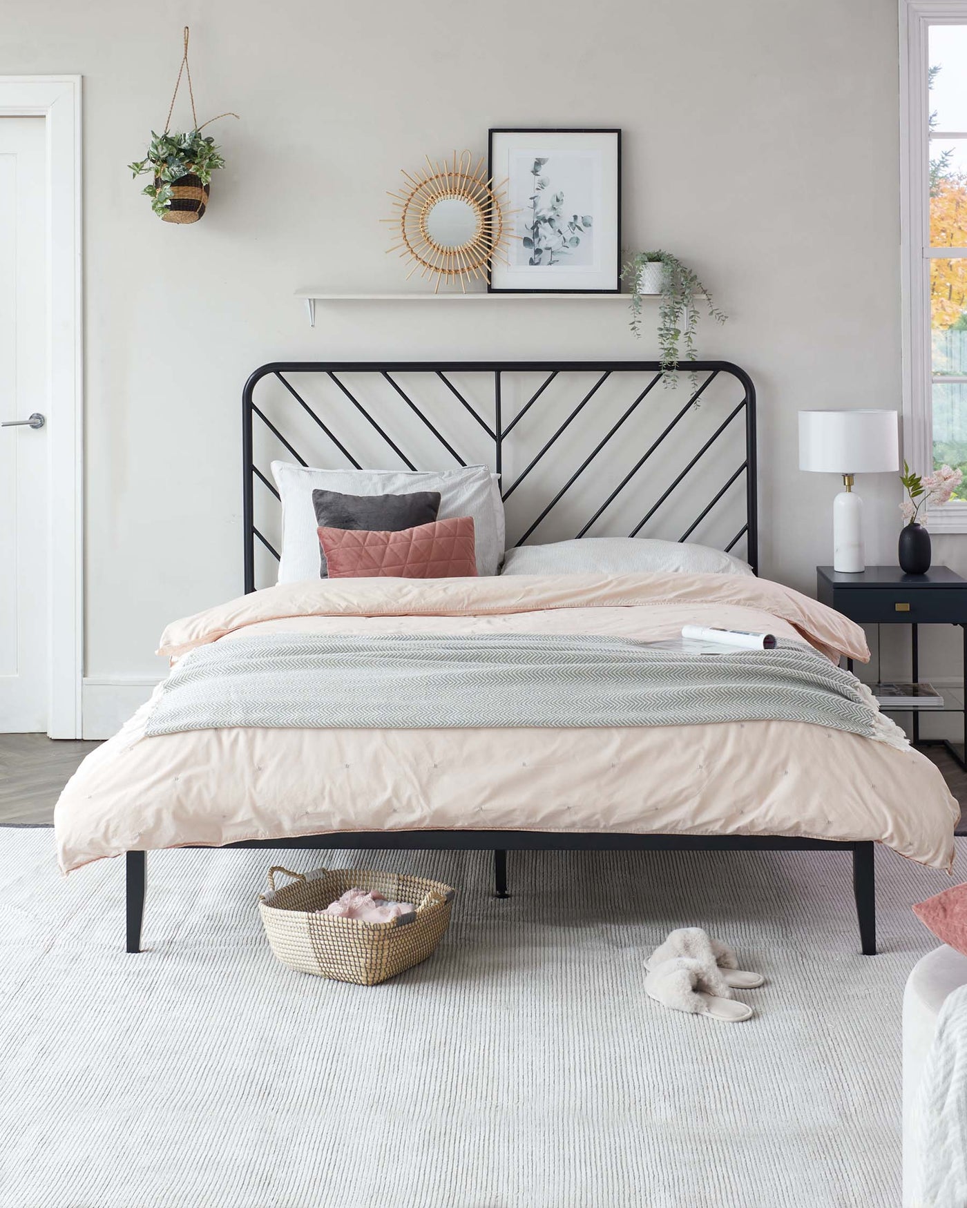 A black metal bed frame with a clean-lined headboard featuring geometric patterns, accompanied by a minimalist black bedside table with a drawer, set on a textured light-coloured area rug.