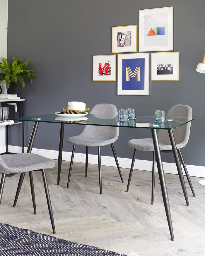 Modern dining area with a rectangular glass-top table on slim black metal legs and four matching grey upholstered chairs with sleek black frames. The setting reflects a contemporary minimalist style.