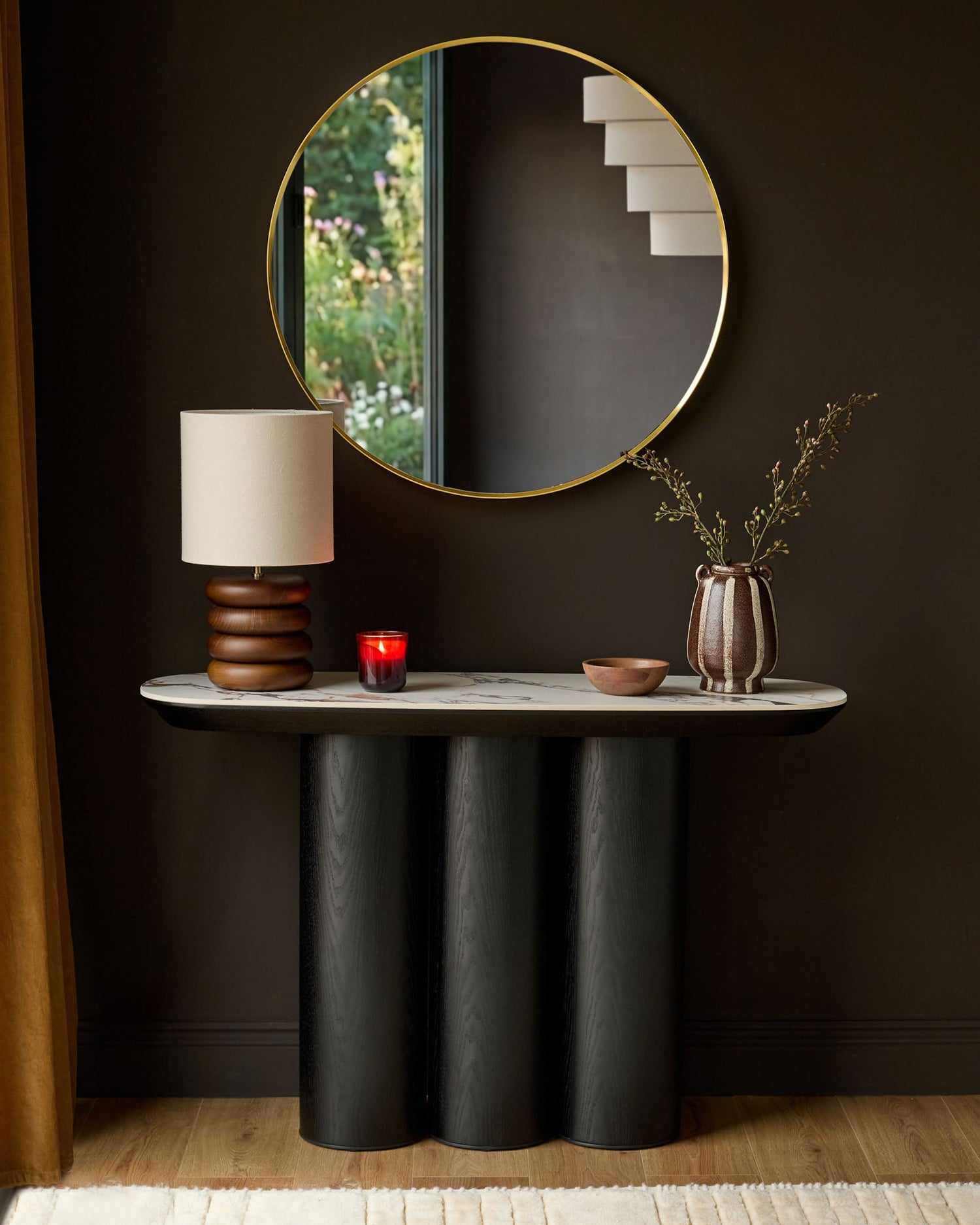 Lena console table in Calacatta white with black cylindrical base, styled with lamp, mirror, and decorative accessories.
