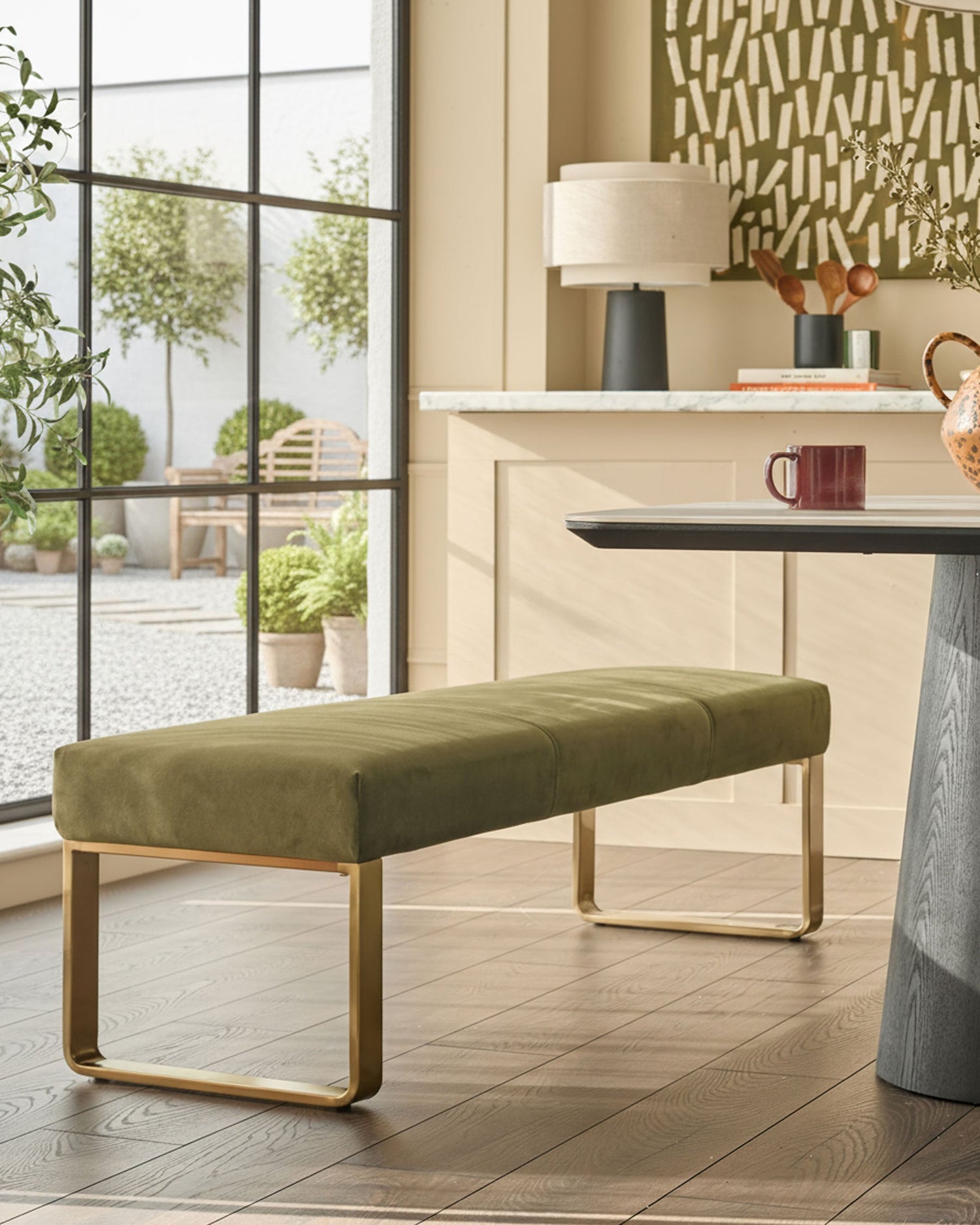 Loop 3-seater velvet bench without backrest in olive green with brushed brass frame, shown in modern room setting.