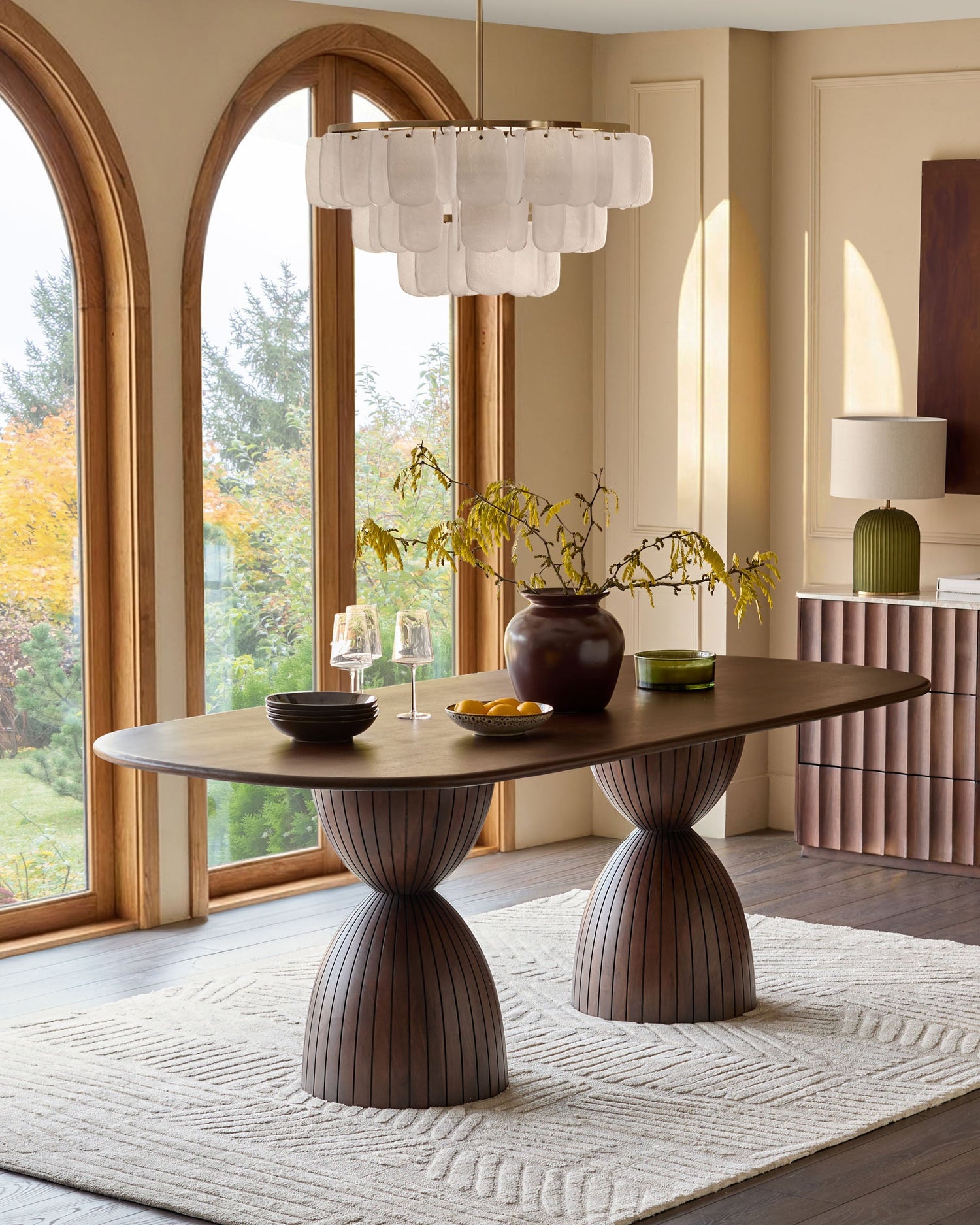 Malin 8-seater dining table in dark mango wood with oval top and fluted pedestal base, styled in a modern dining room.