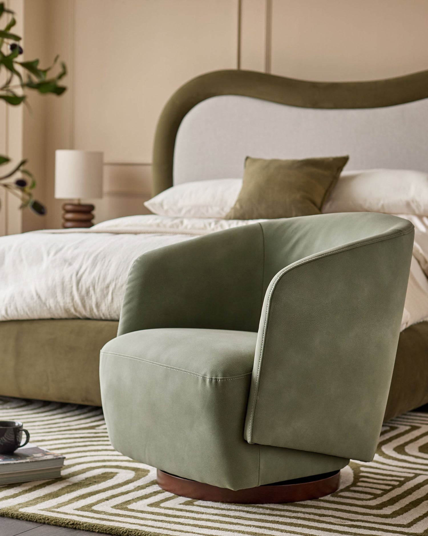 Sage green faux leather swivel chair with curved back and wooden base in bedroom setting.