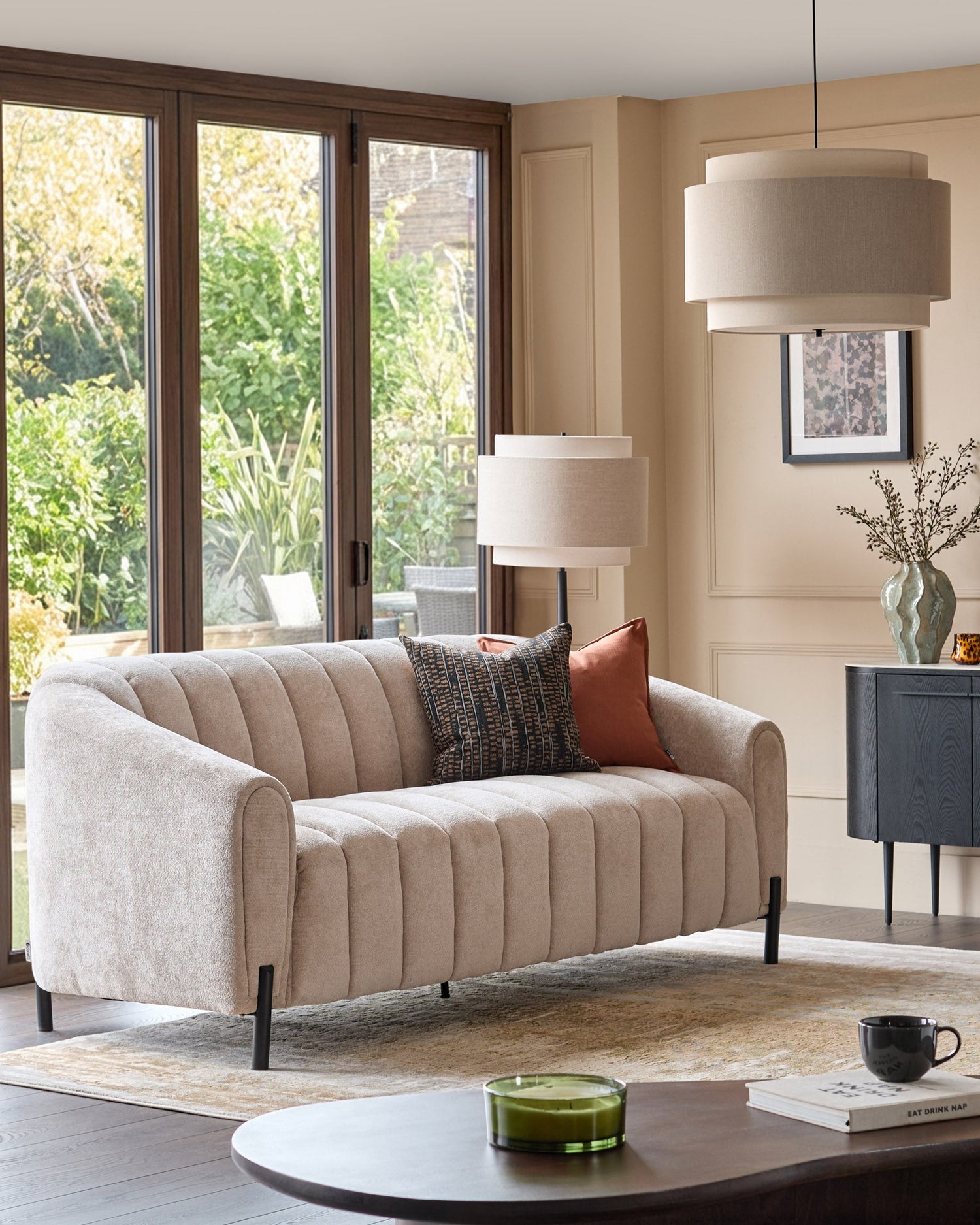 Kendra 3-seater sofa in natural fabric with vertical channel quilting, black metal legs, displayed in a modern living room setting.