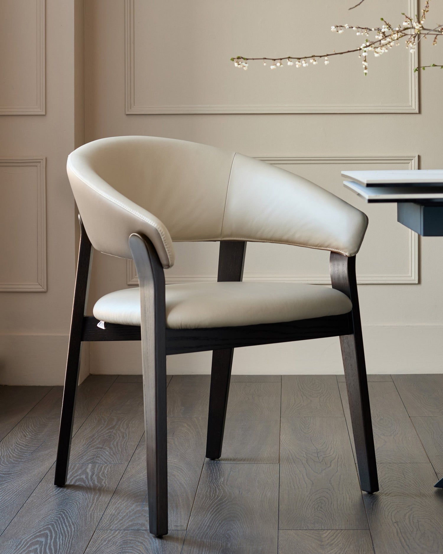 Amelia dining chair in natural leather with mocha wood frame, curved backrest, shown in modern room setting.
