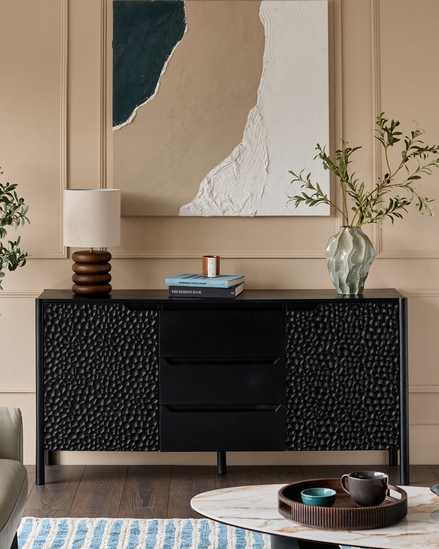 Black wood sideboard with textured hammered panel doors and central drawers, displayed in a styled living room setting.