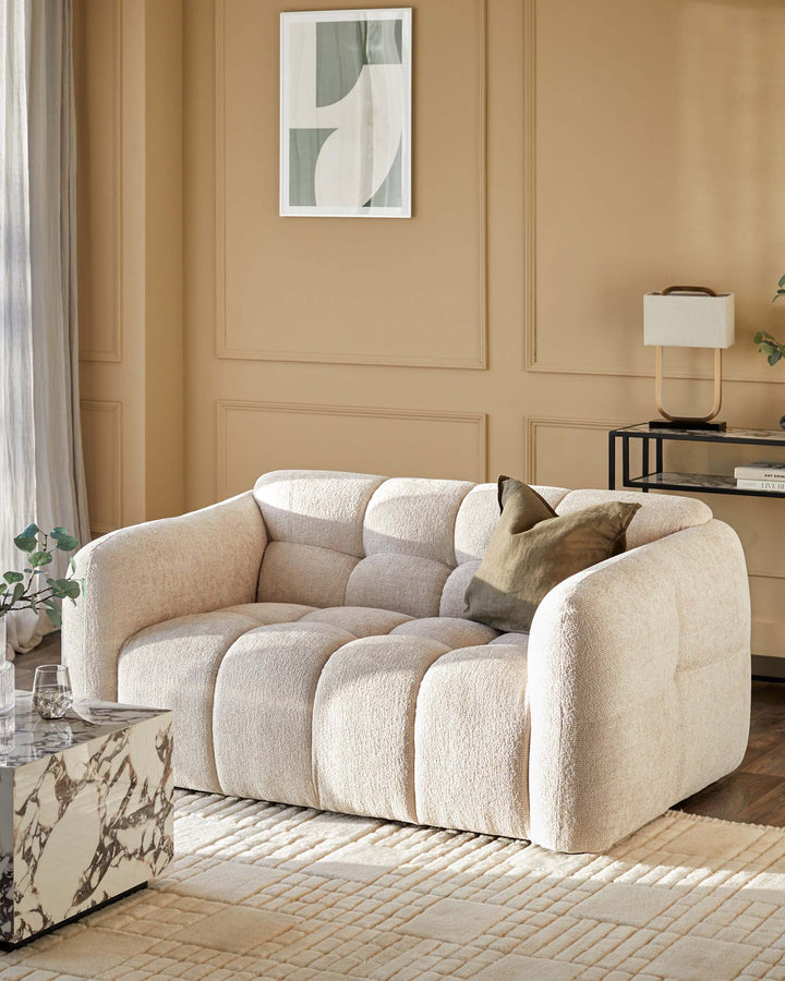 A cosy, cream-coloured sofa with a buttoned design, complemented by neutral decor and a textured rug.