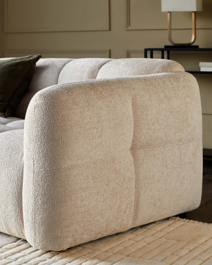 Close-up of a cream, textured sofa with a dark green cushion and a black side table with a lamp.