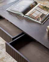A dark wood veneer coffee table with 2 drawers partially open. An open magazine rests on top.