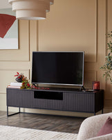 A dark wood TV stand with grooved doors, supporting a flatscreen TV. Accessories include a vase, books and candle.