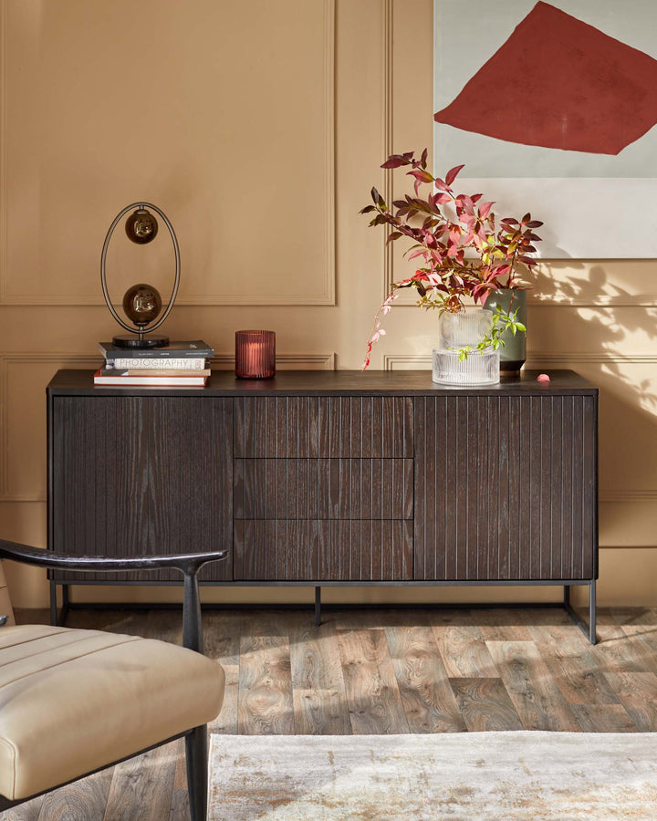 Stylish dark wood sideboard with sleek metal legs, adorned with books, a lamp, candles, and decorative vases.
