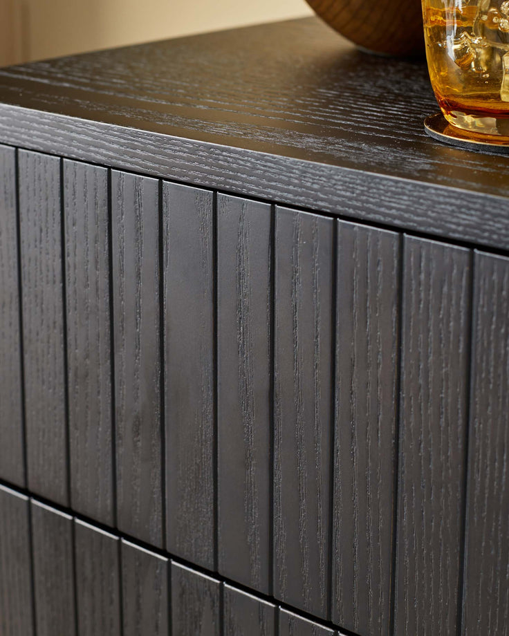Close-up of a modern black wood cabinet with reeded drawer fronts, showcasing its texture and design.