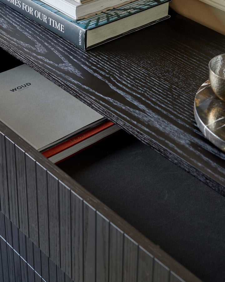 Close-up of a dark wood unit with books and a tray on top, and a drawer partially open.