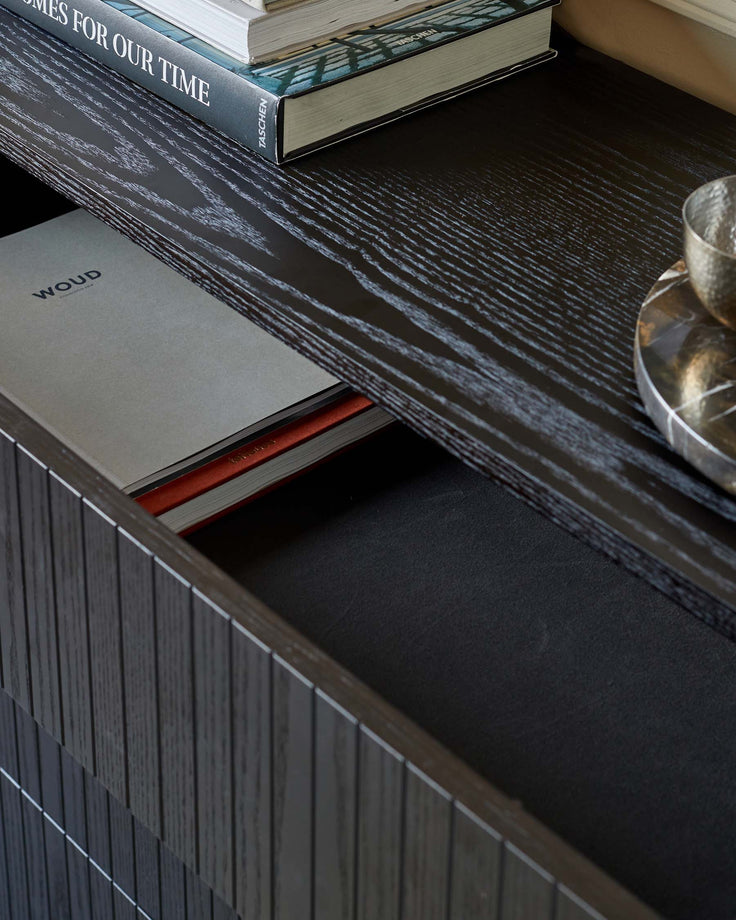 Close-up of a dark wood unit with books and a tray on top, and a drawer partially open.